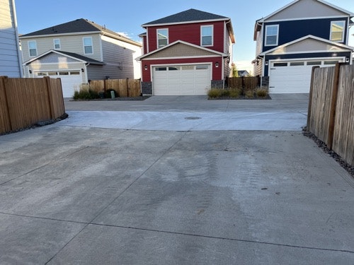 A residential area with houses, driveways, and a fence under a clear sky.