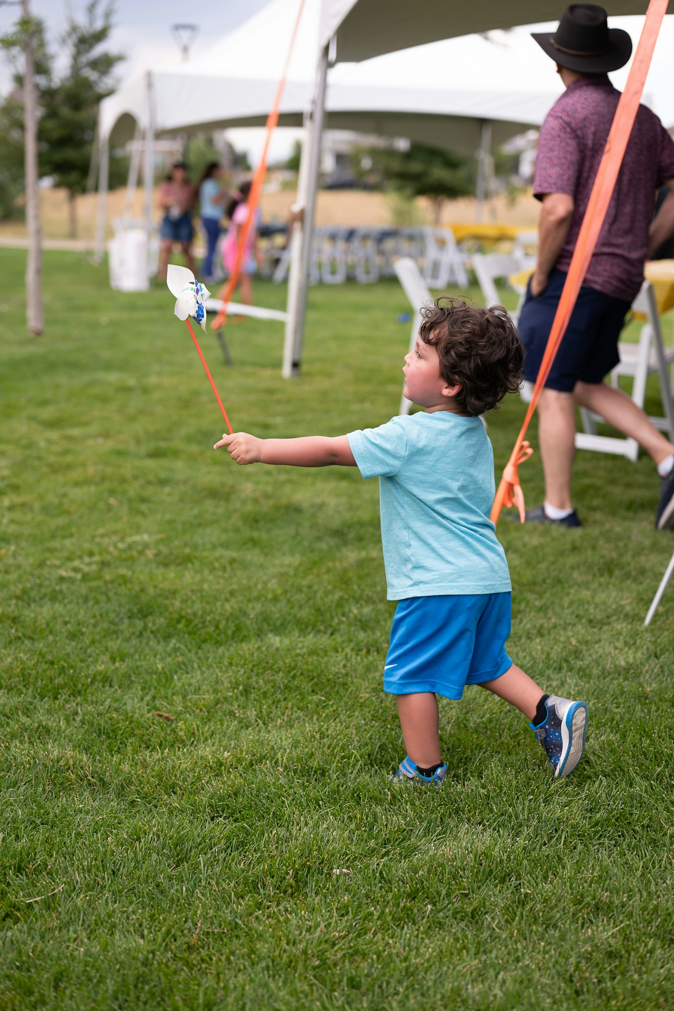 Child in blue outfit joyfully playing with a pinwheel outdoors near tents.
