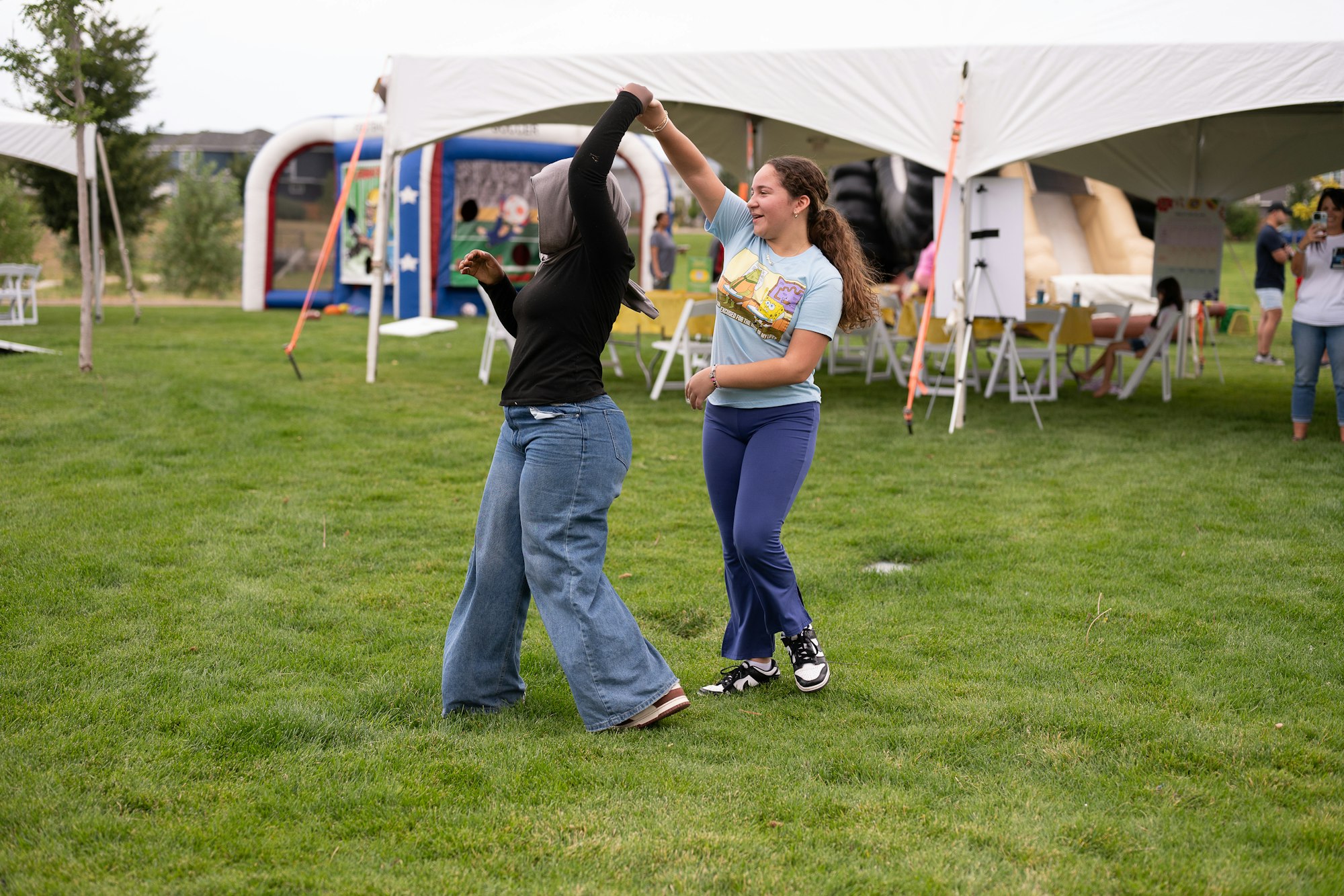 Two people dancing on grass at an outdoor event with tents and inflatables in the background.