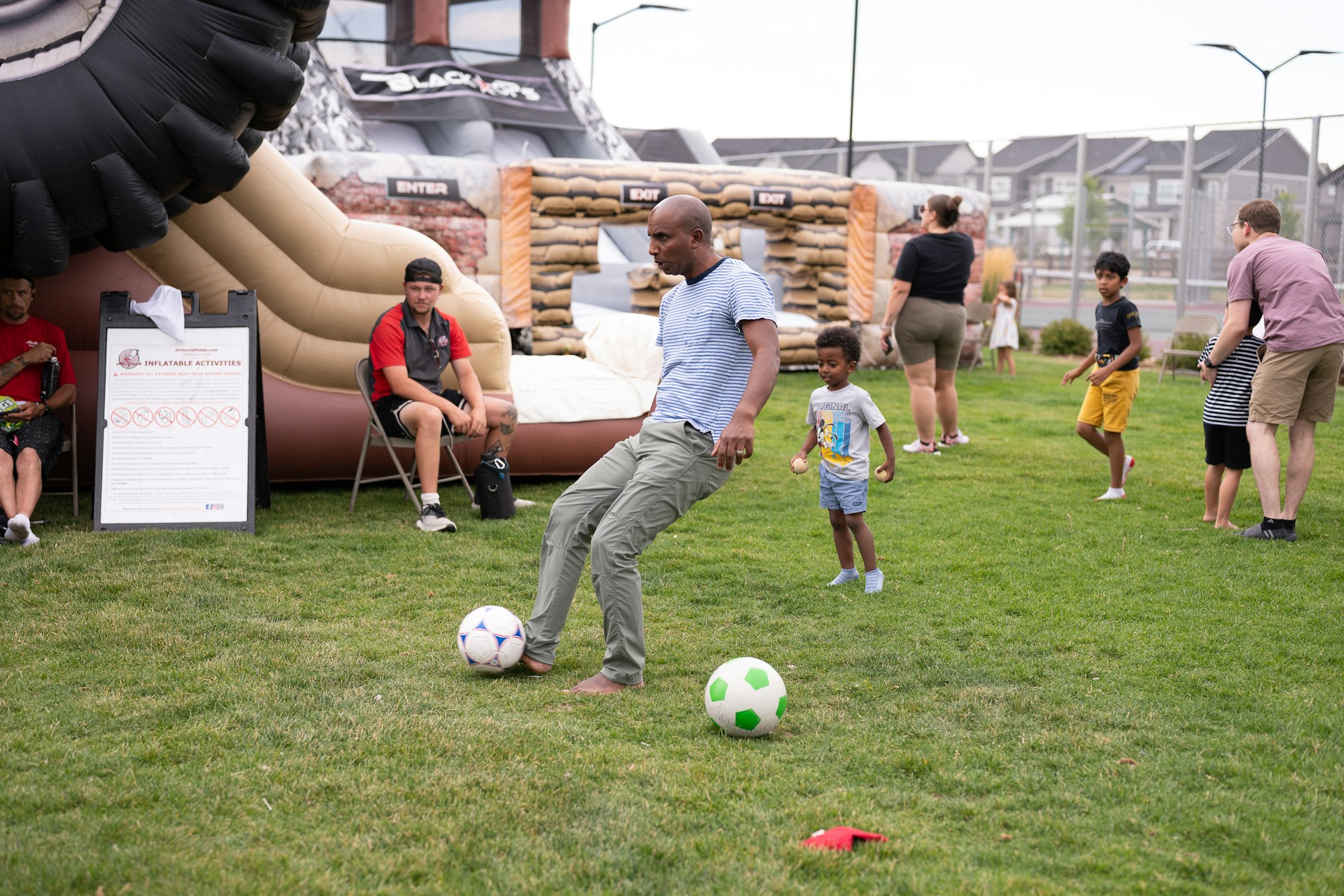 People playing on grass with inflatable activity in the background, surrounded by families and kids.