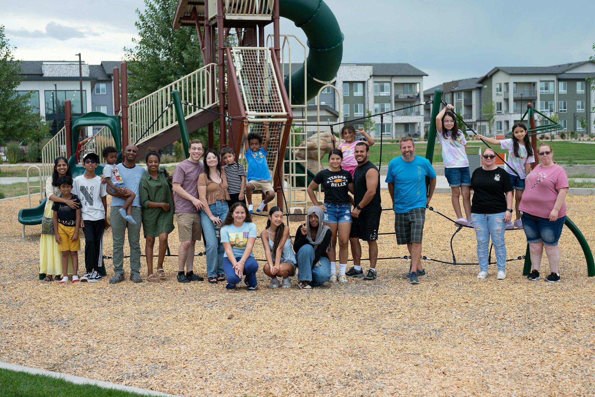 A group of people, including children, posing together at a playground with slides and climbing structures.