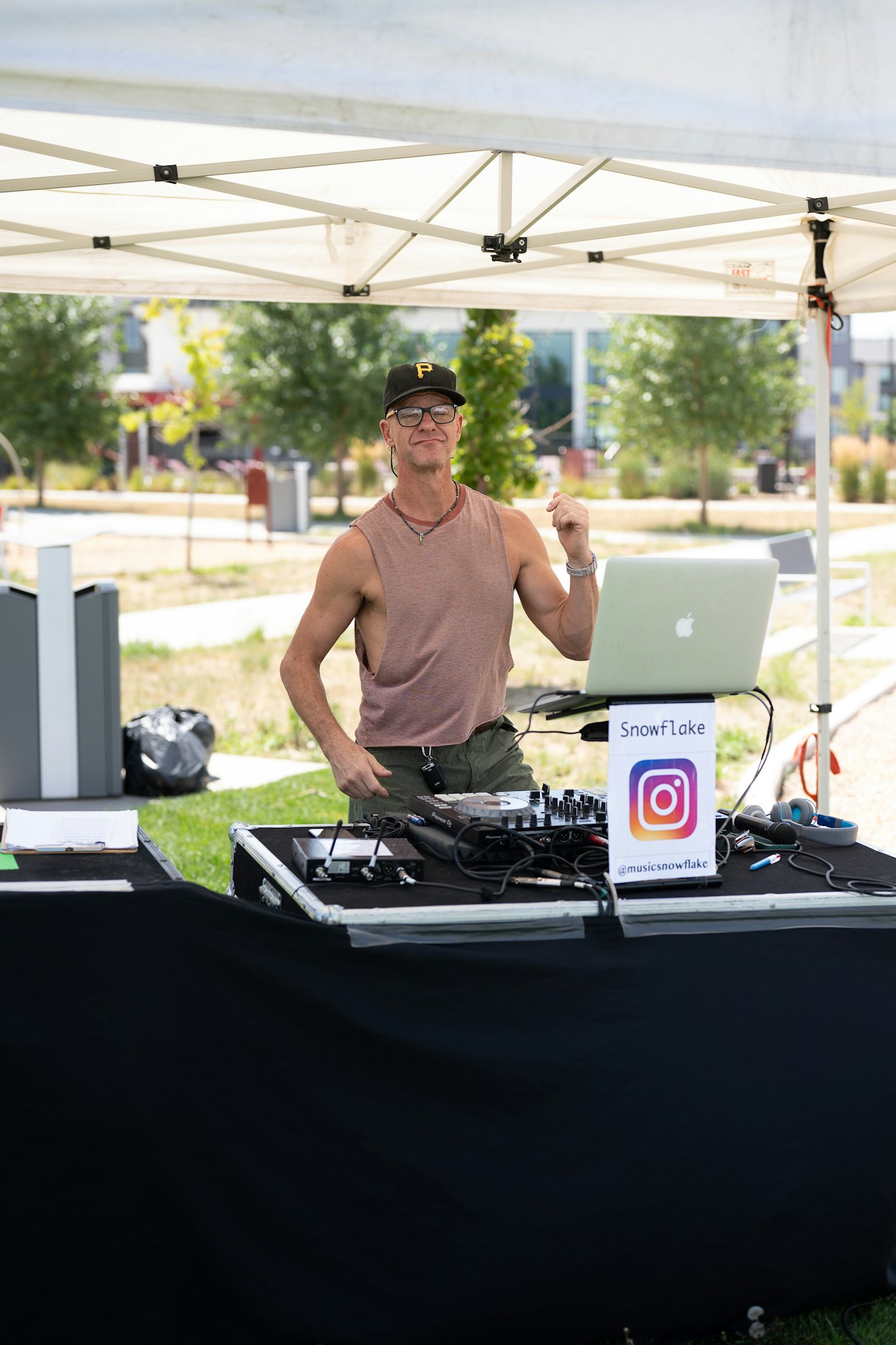 A person DJing under a tent with equipment set up and an Instagram sign on the table.