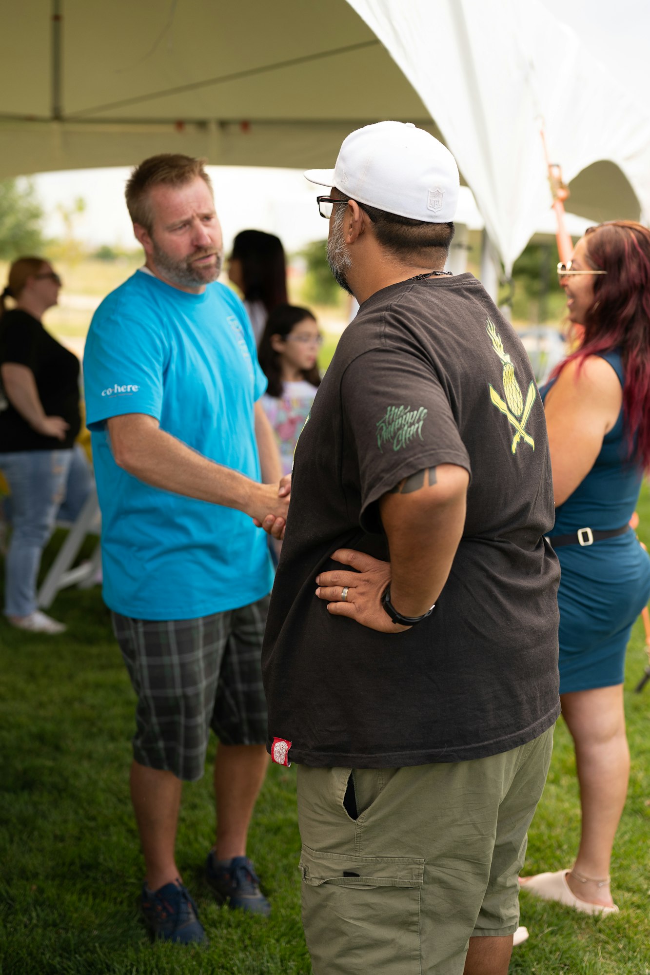 Two men shaking hands outdoors at an event with people in the background.