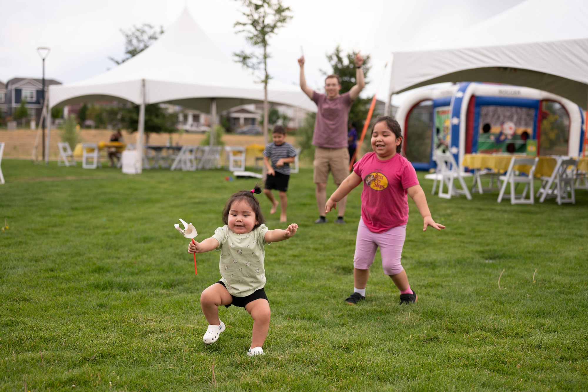 Children playing joyfully on a grassy lawn with tents in the background.