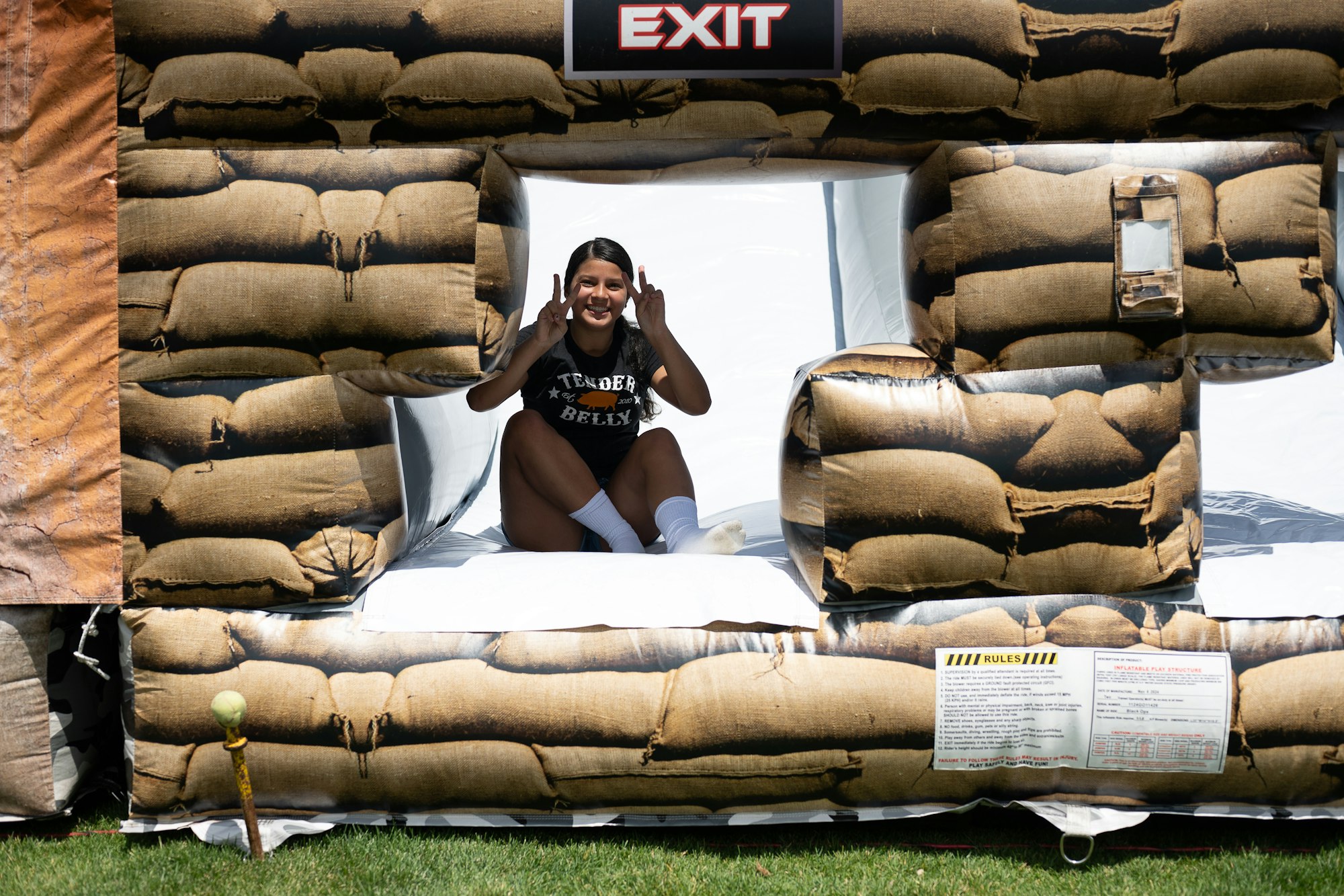 Person sitting in an inflatable structure's exit, smiling and making peace signs.