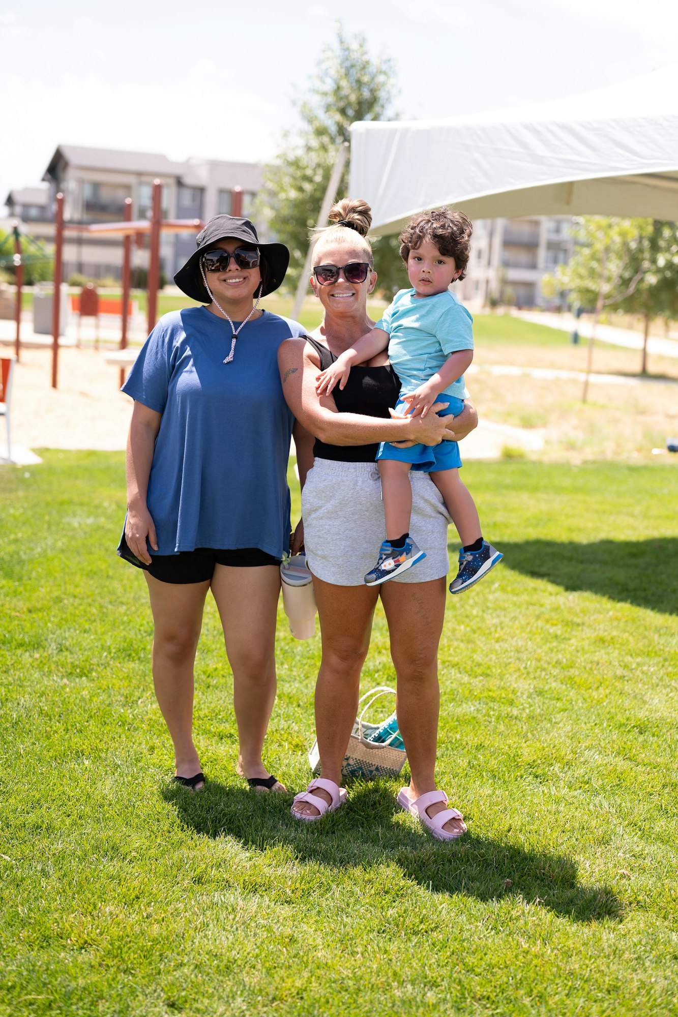 Two adults and a child standing on grass at an outdoor park on a sunny day.