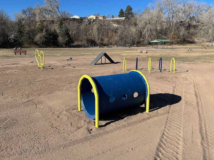 Outdoor dog agility park with hoops, tunnel, and obstacles on a sandy area.