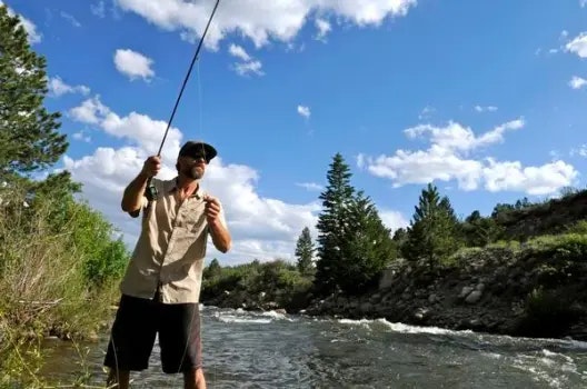 A man fishing by a river, surrounded by nature.