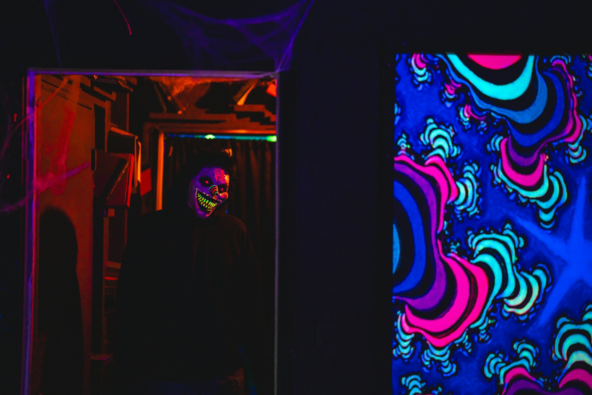 Creepy clown mask in dim lighting, blacklight art with vibrant, psychedelic patterns.