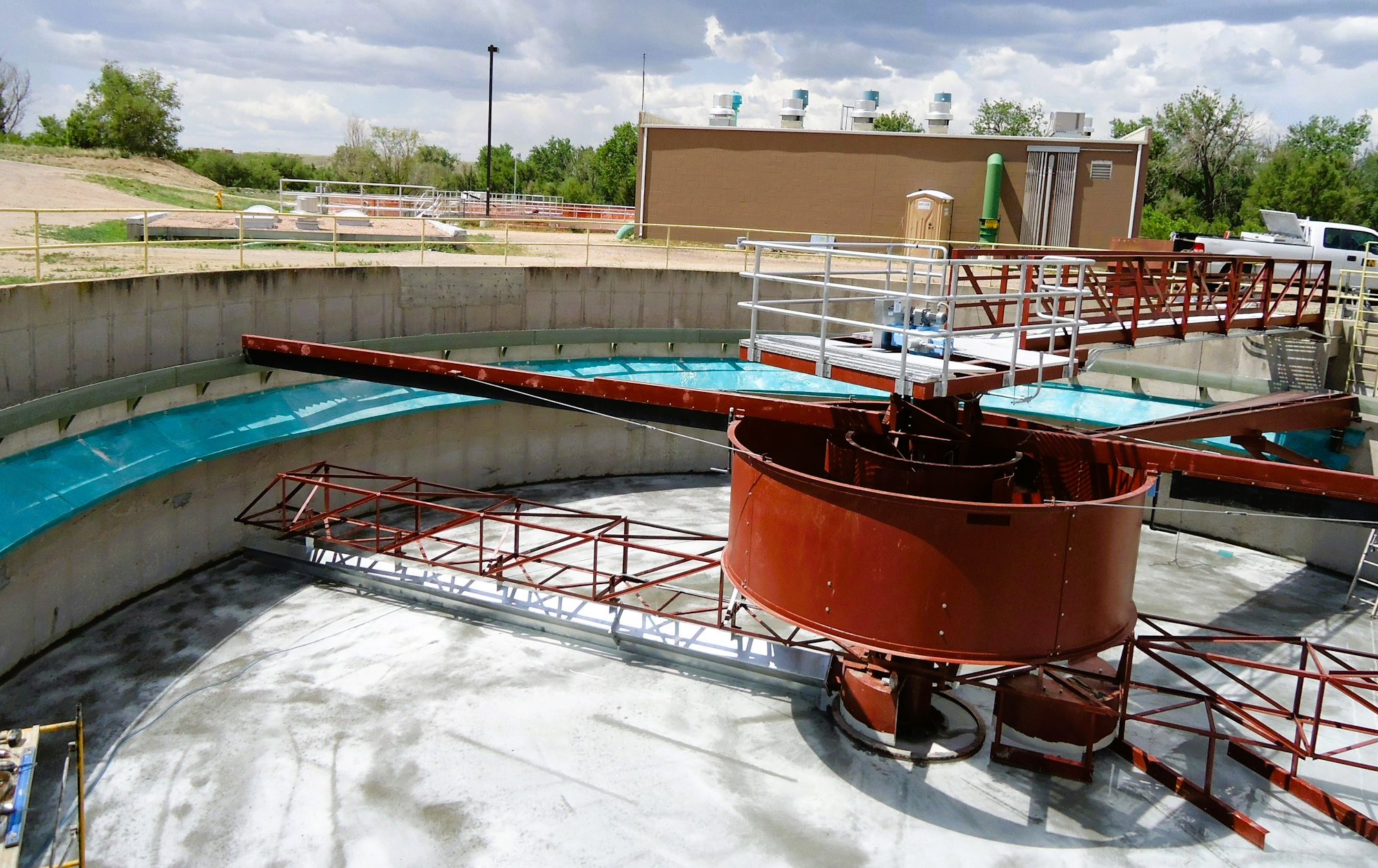 Wastewater treatment facility with a circular clarifier and mechanical arm, surrounded by outdoor equipment and buildings.