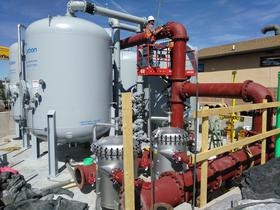 Industrial equipment with tanks, pipes, and a worker on a lift, likely part of a processing or filtration system.