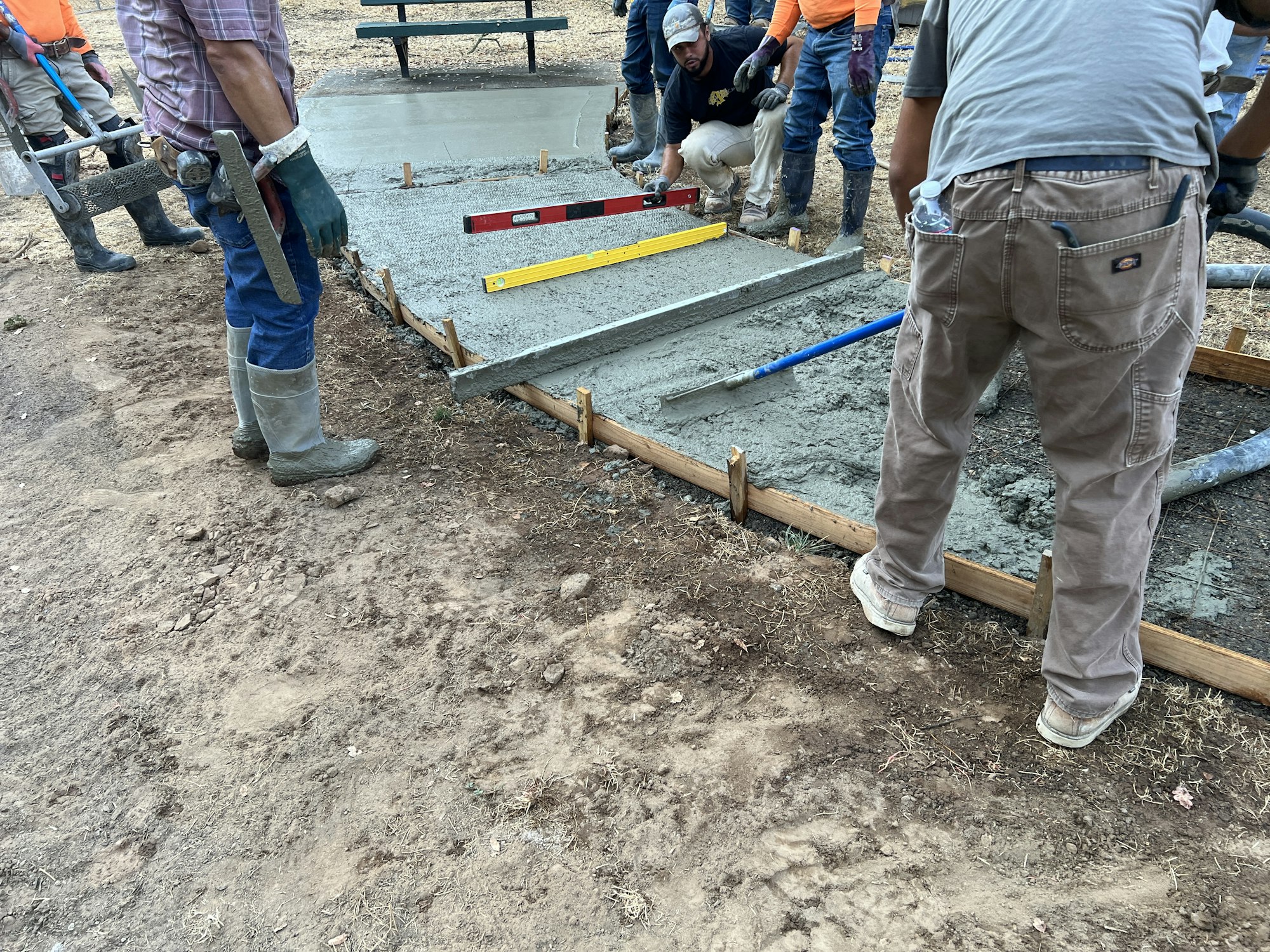 Workers leveling fresh concrete with tools and a spirit level, constructing a slab outdoors.