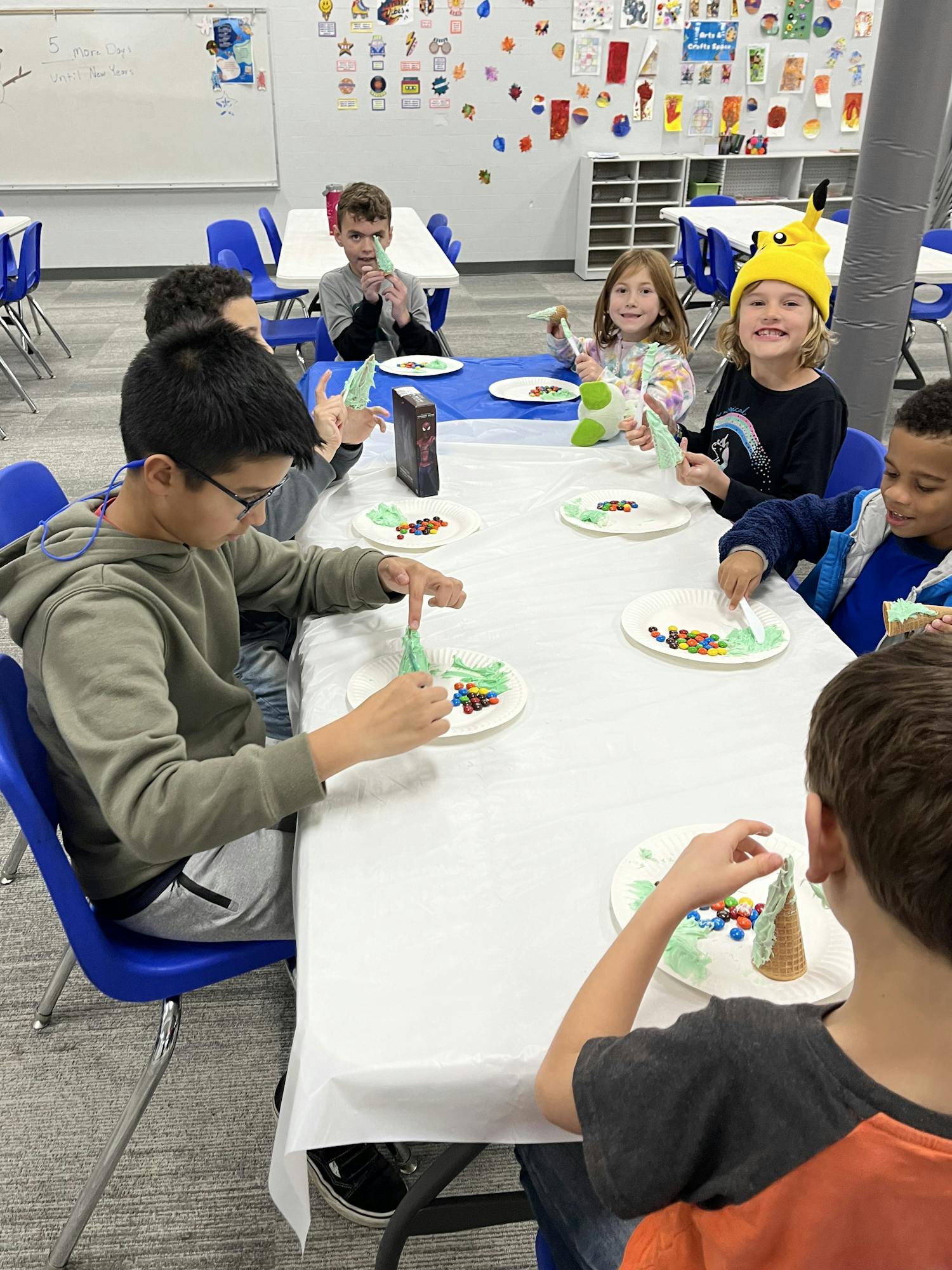 Kids crafting with candy and cones at a table in a colorful classroom.