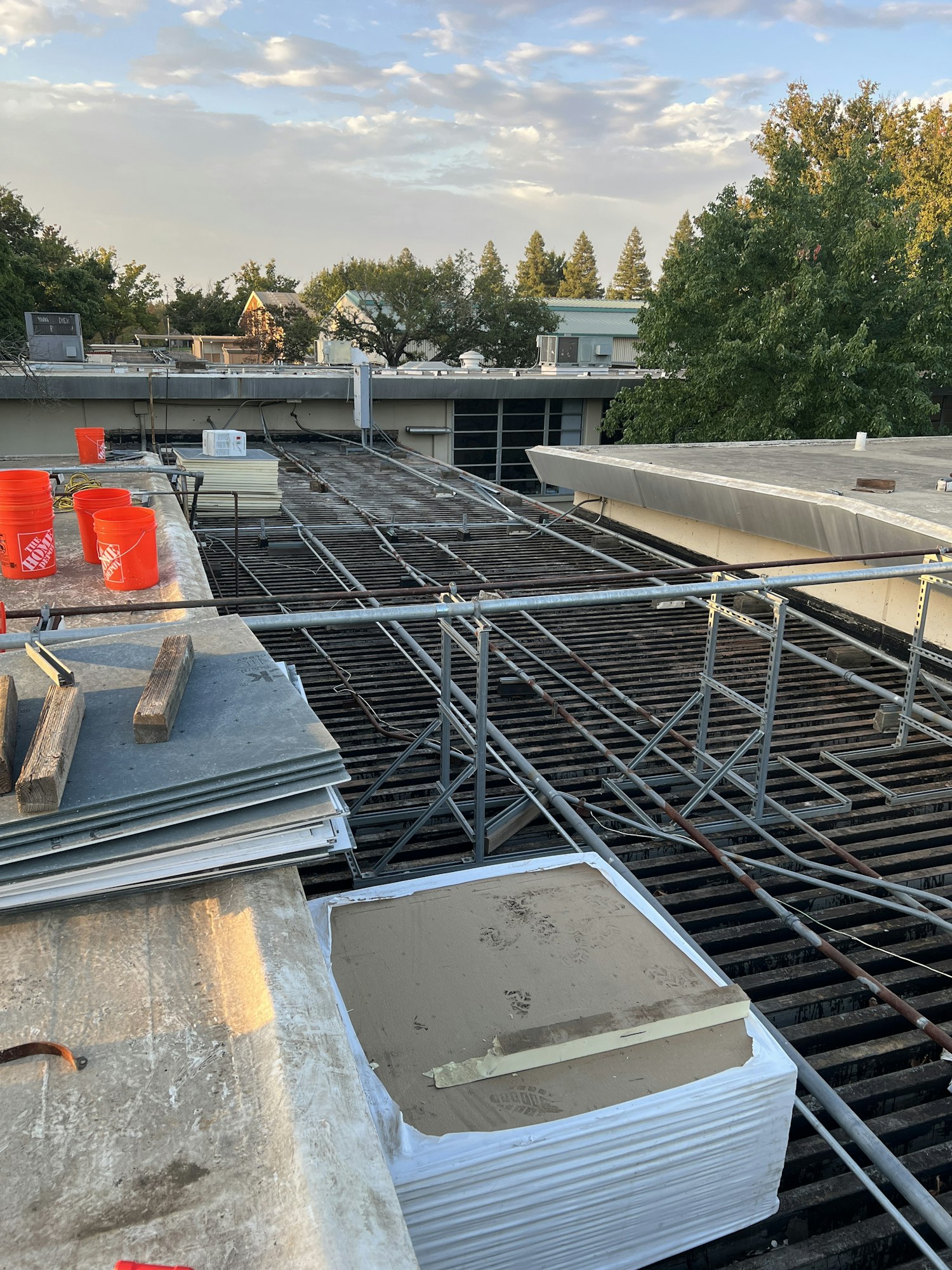 Construction materials and tools on a rooftop with trees and sky in the background.