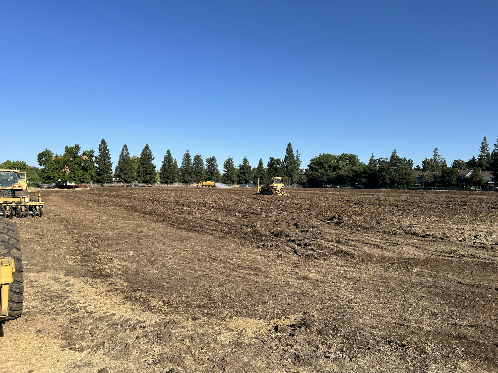 A construction site with heavy machinery on a clear day, surrounded by trees.