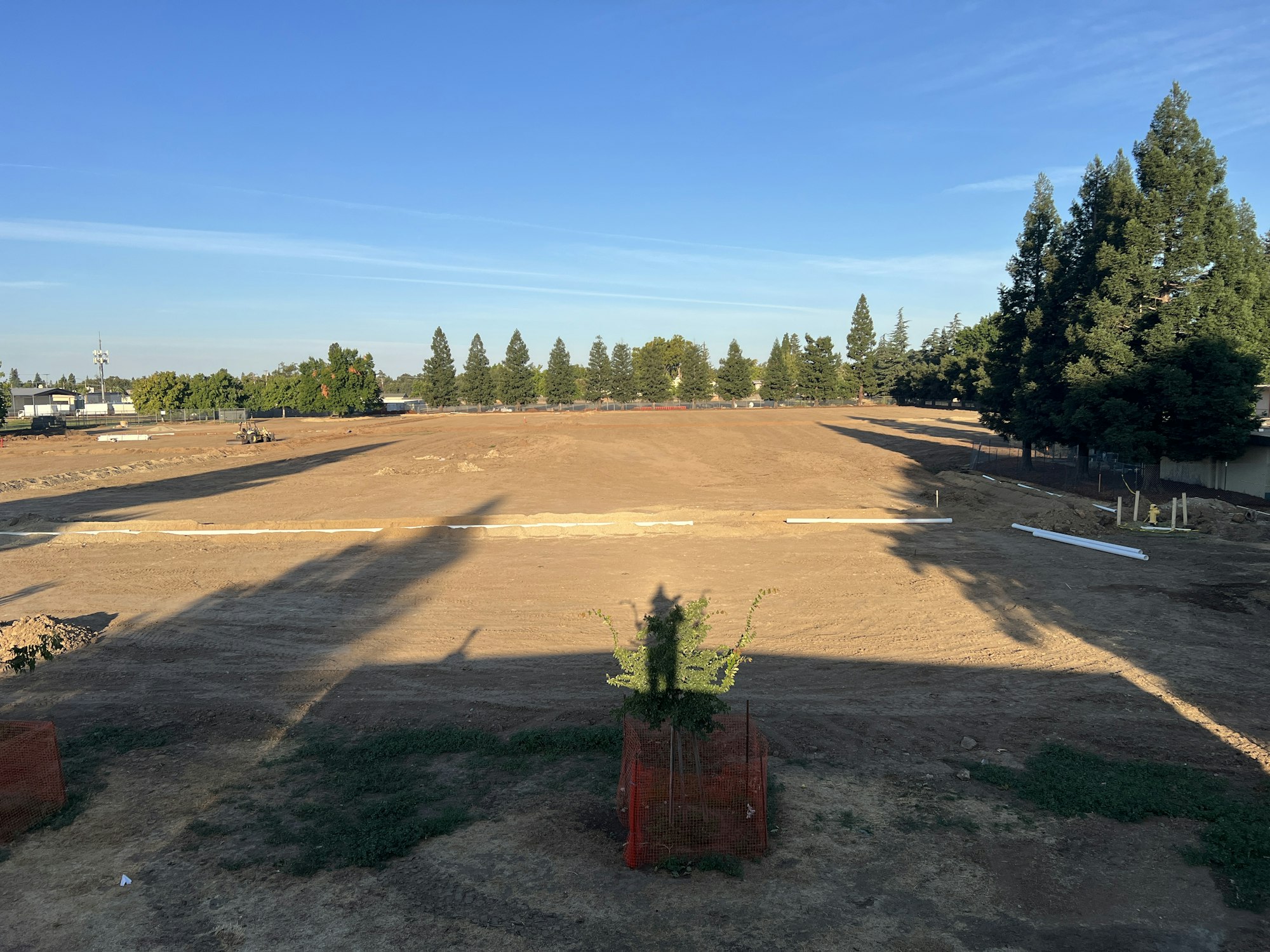 A large open dirt field under a clear blue sky, surrounded by trees.