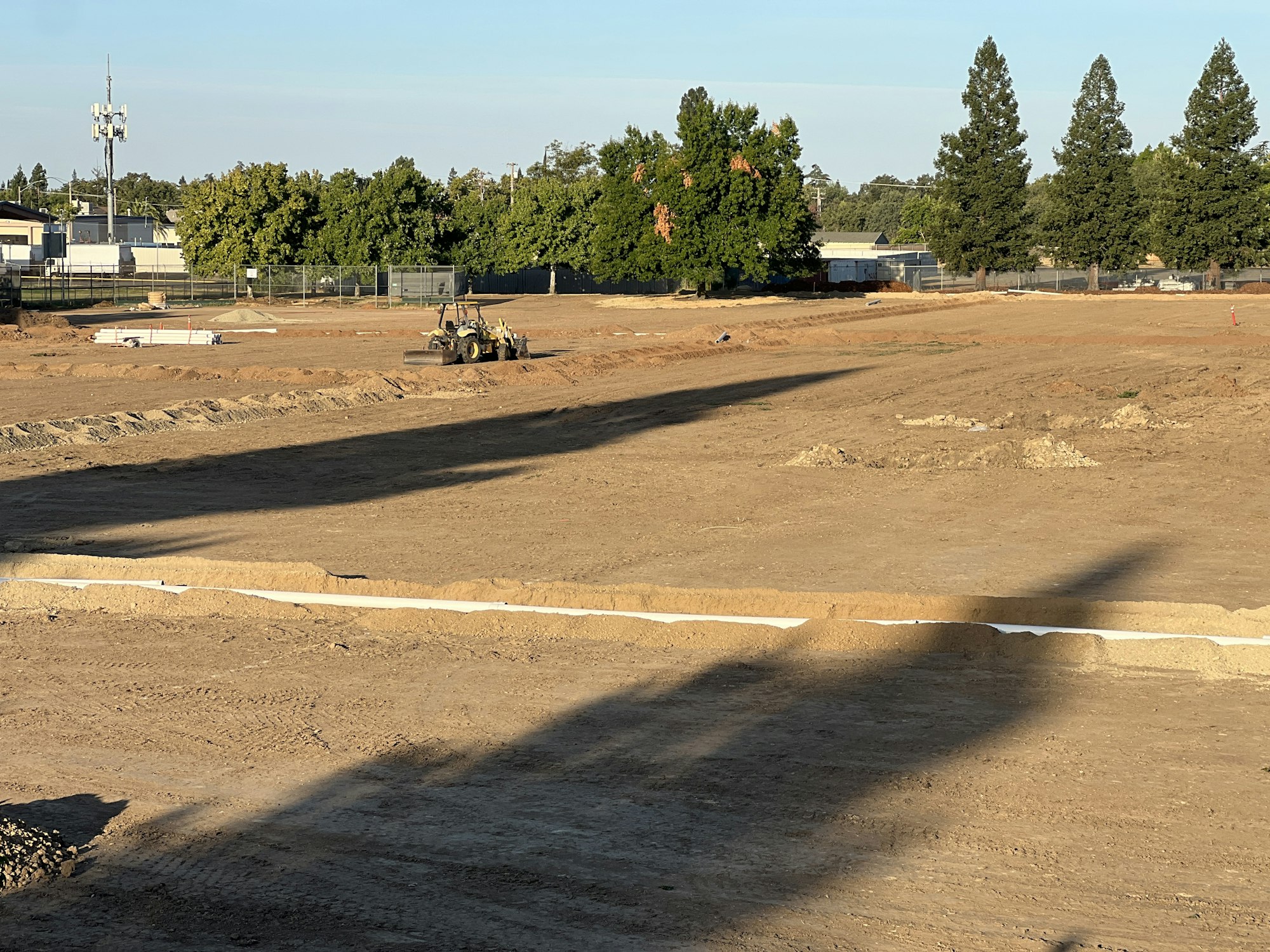 A construction site with a tractor, dirt piles, and trees in the background.