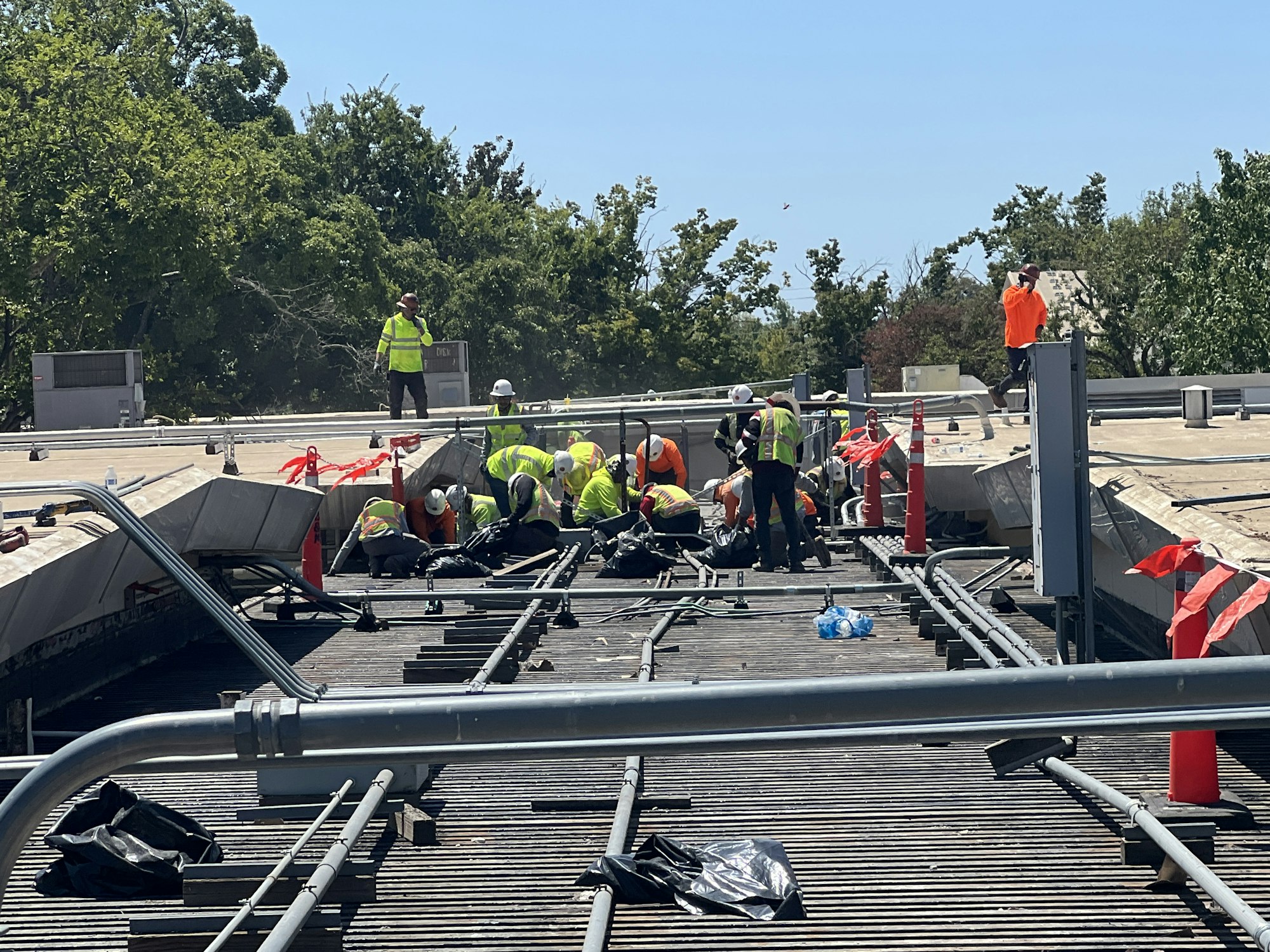 Construction workers in safety gear working on a rooftop with trees in the background.