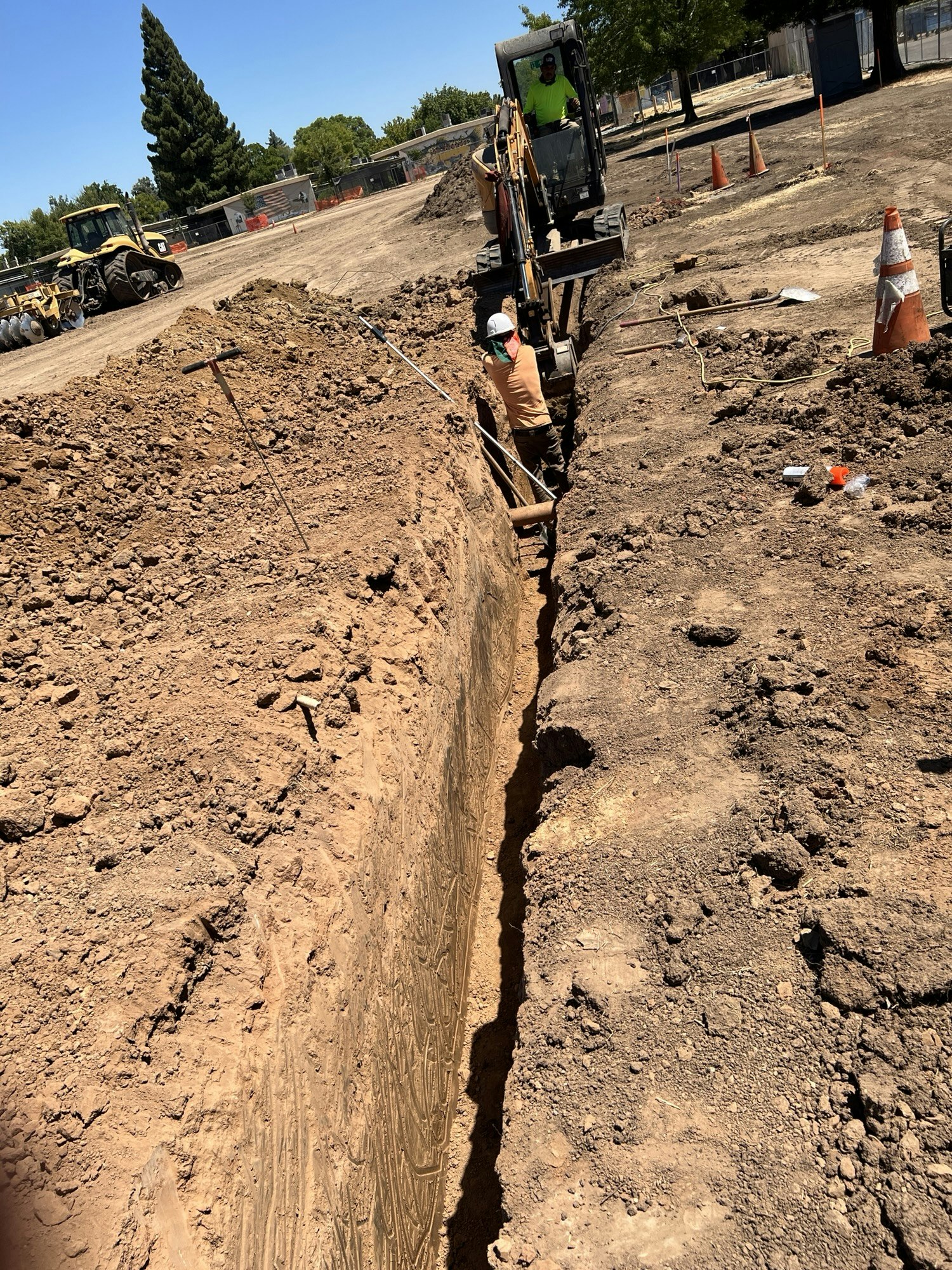 Construction site with a worker in a trench and a mini excavator digging nearby.