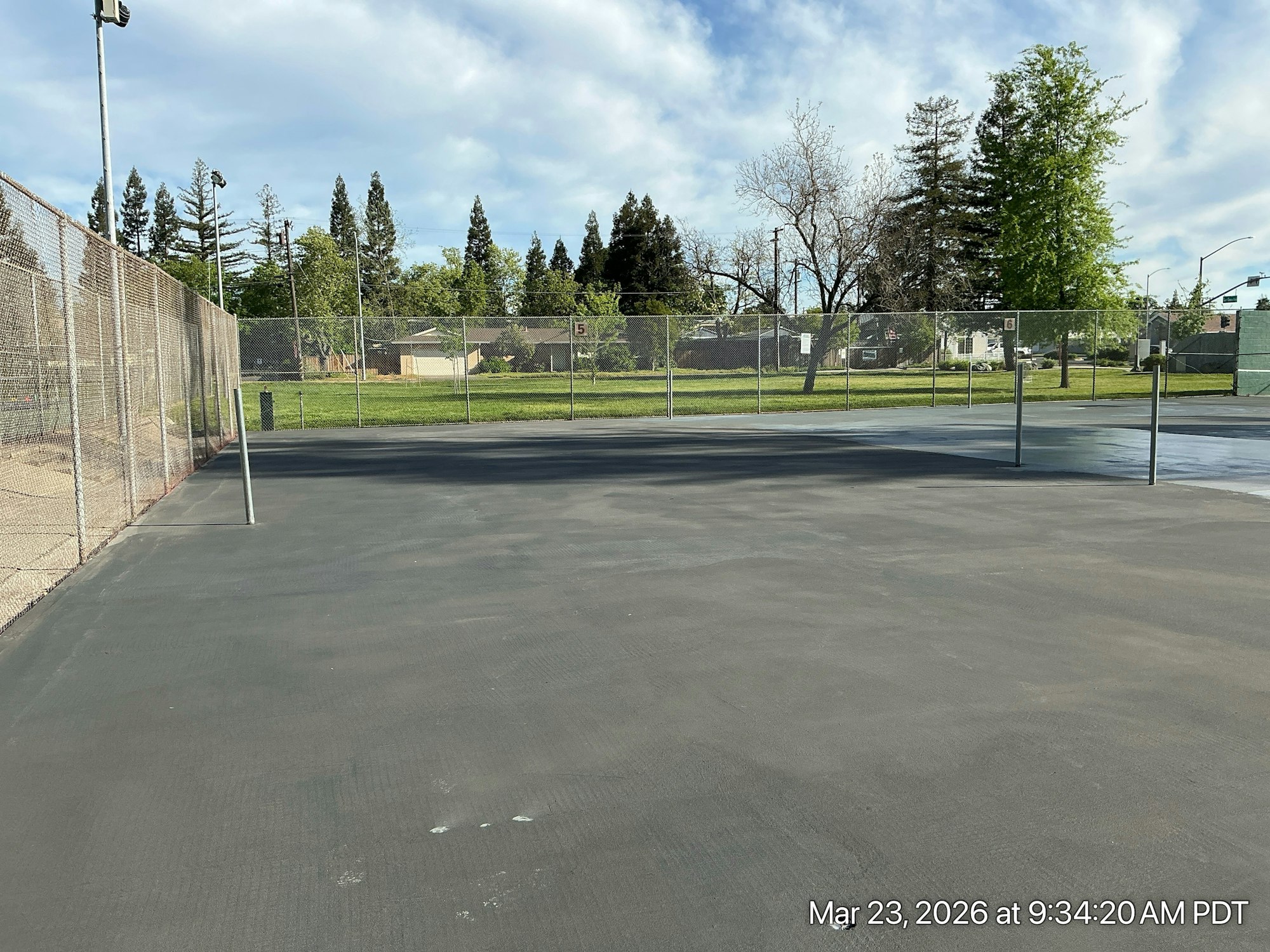 A fenced tennis or sports court with a clear sky, grass area, and trees in the background.