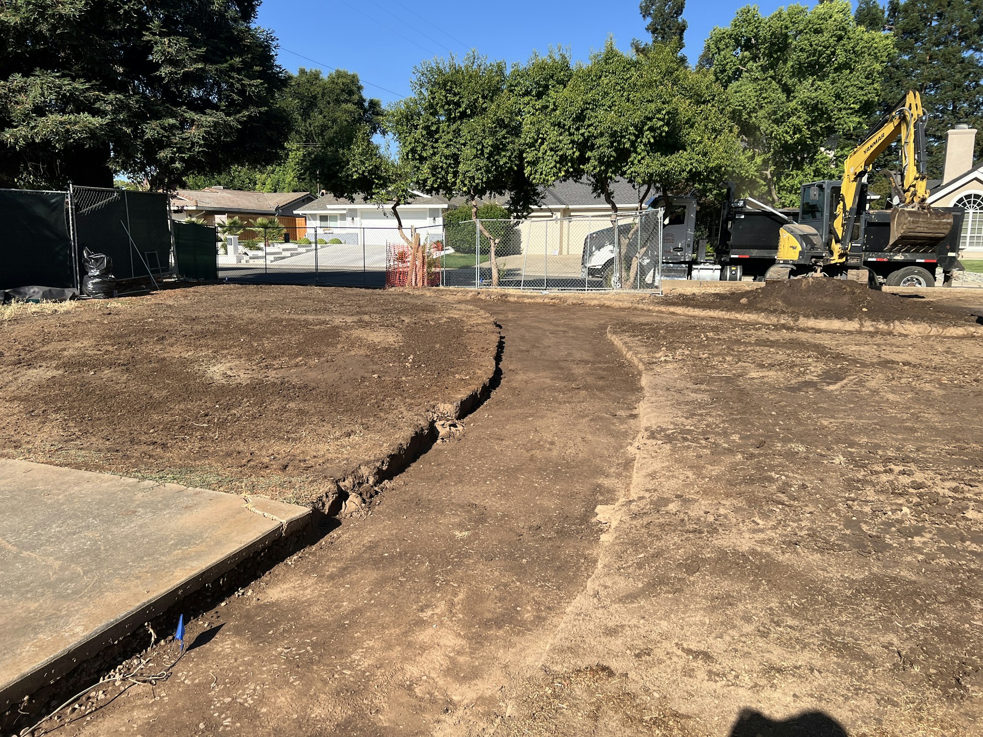 A construction site with excavated dirt, a digger, and protective fencing surrounding the area.