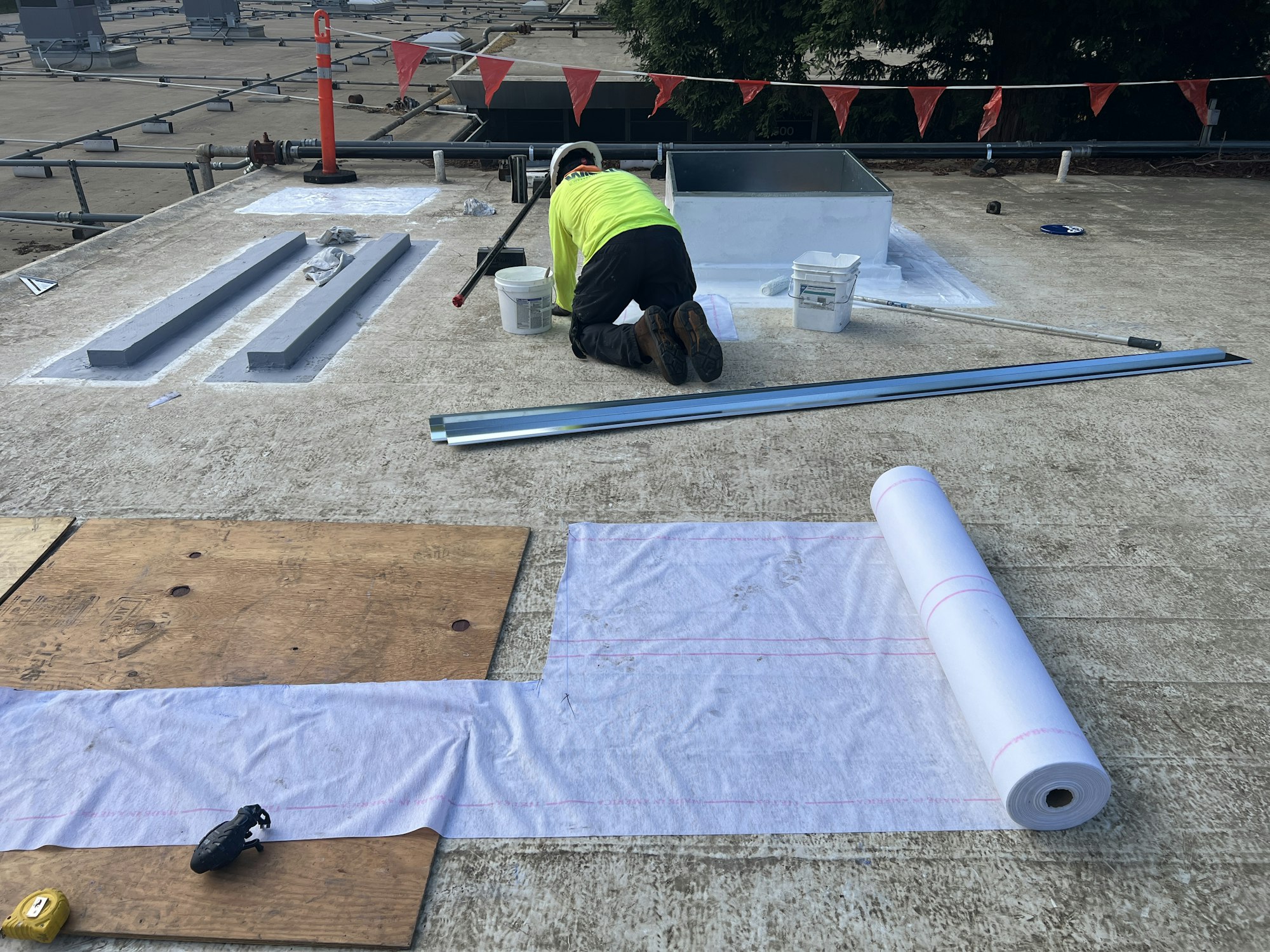 A person working on a rooftop, surrounded by tools, materials, and safety markers.