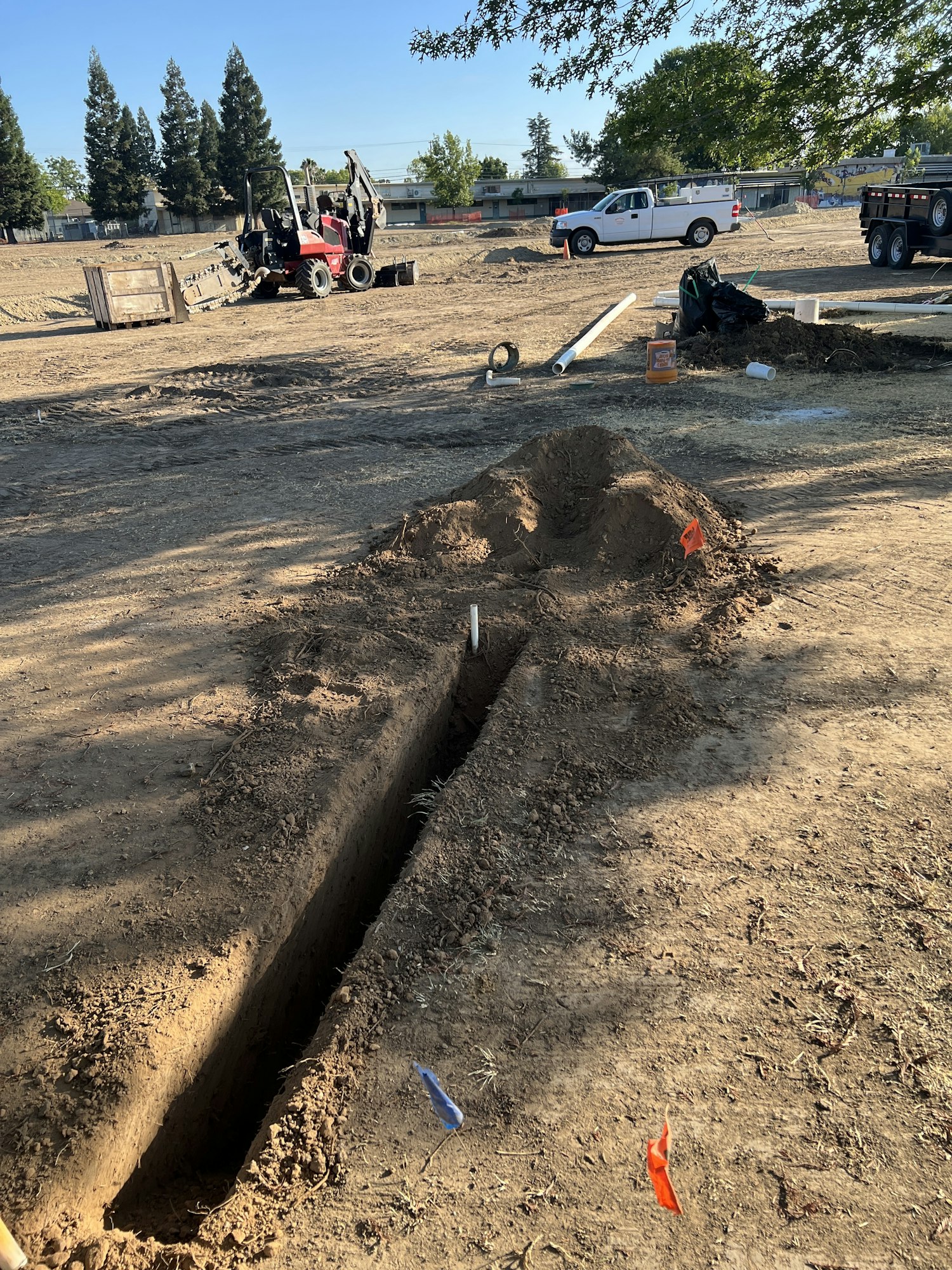 A construction site with a trench, digger, pipes, and a truck.