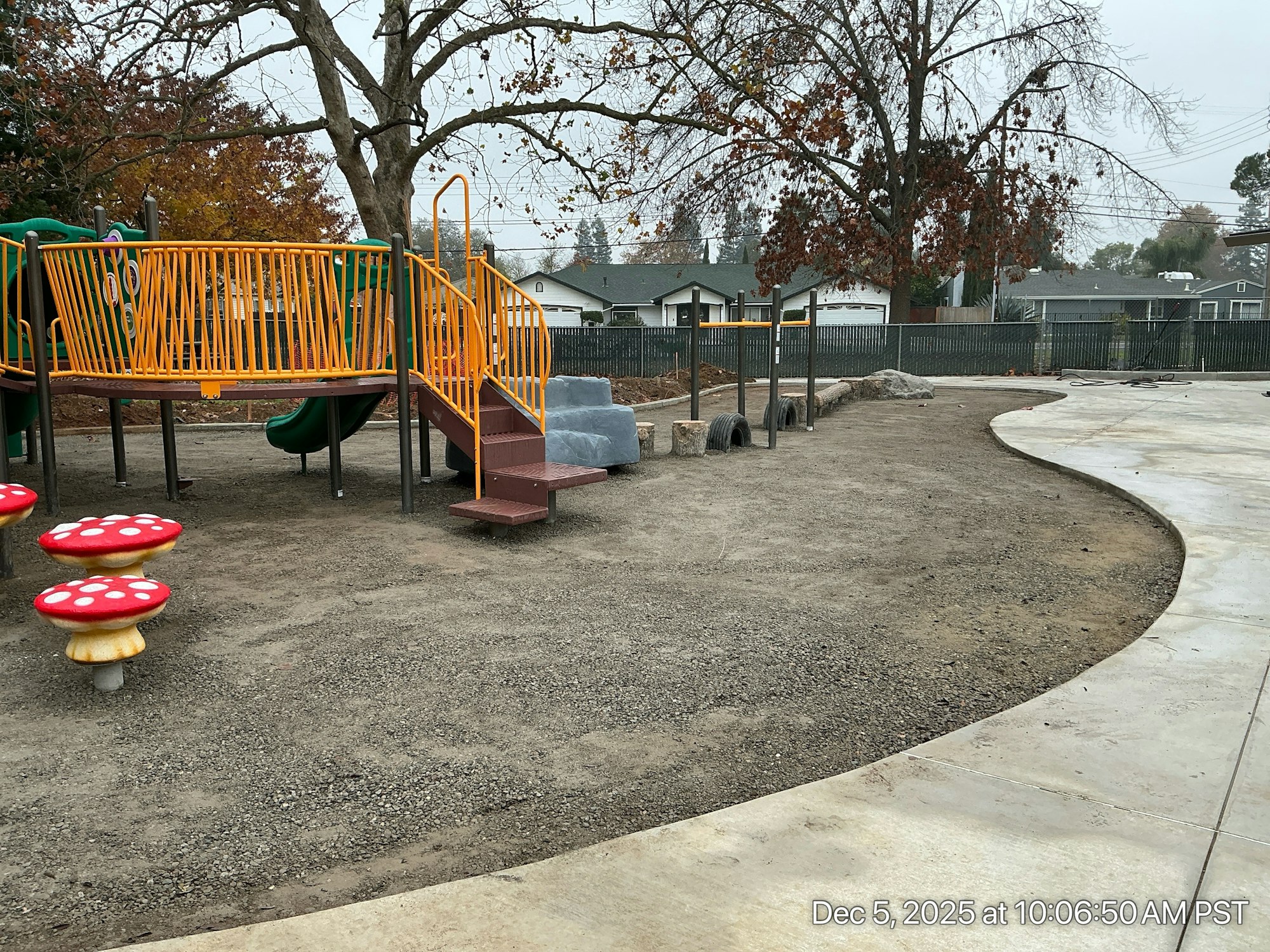 An empty playground featuring colorful play structures, slides, and whimsical mushroom-shaped seating under a cloudy sky.