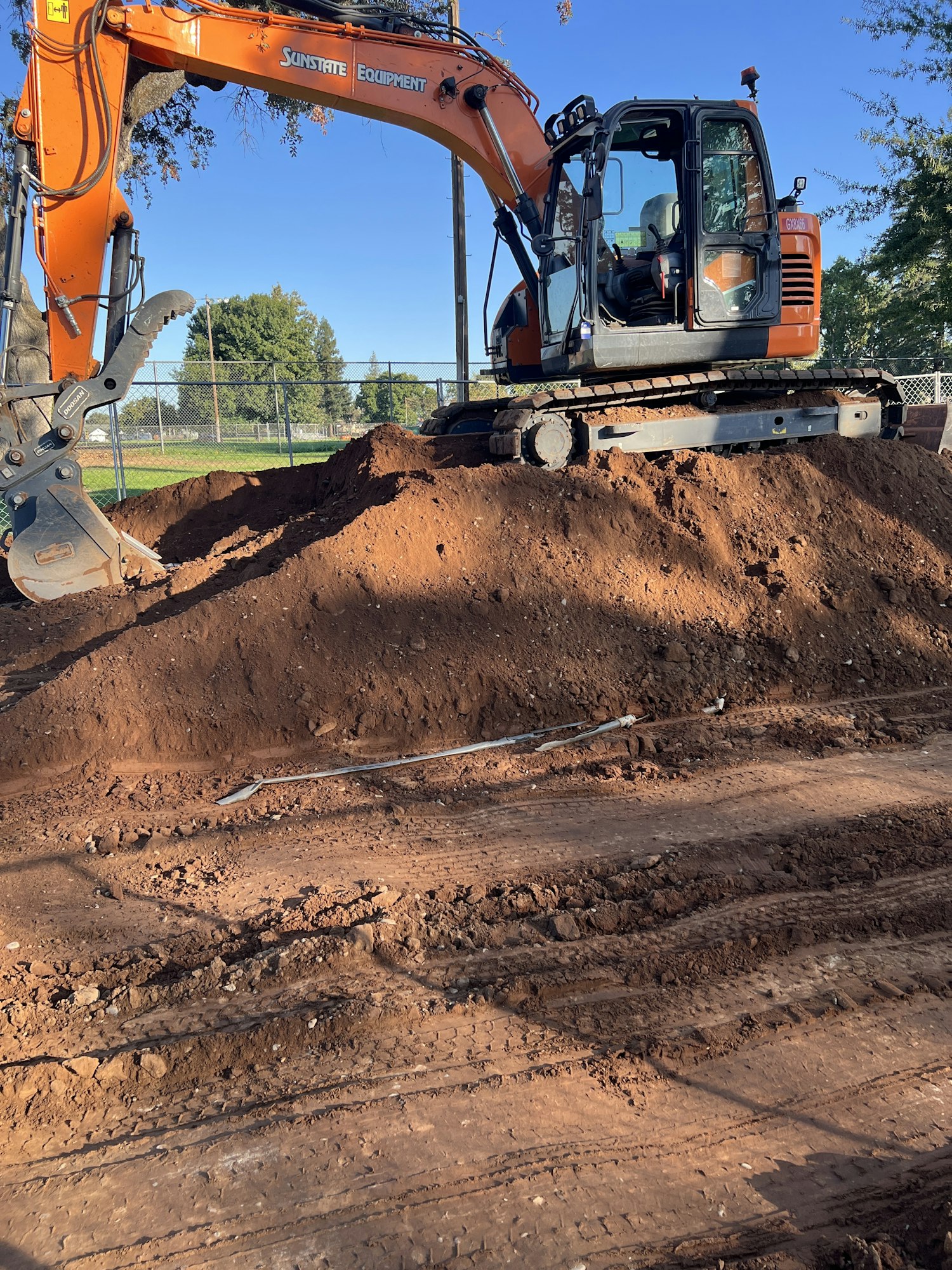 An excavator on a mound of dirt at a construction site with clear skies in the background.