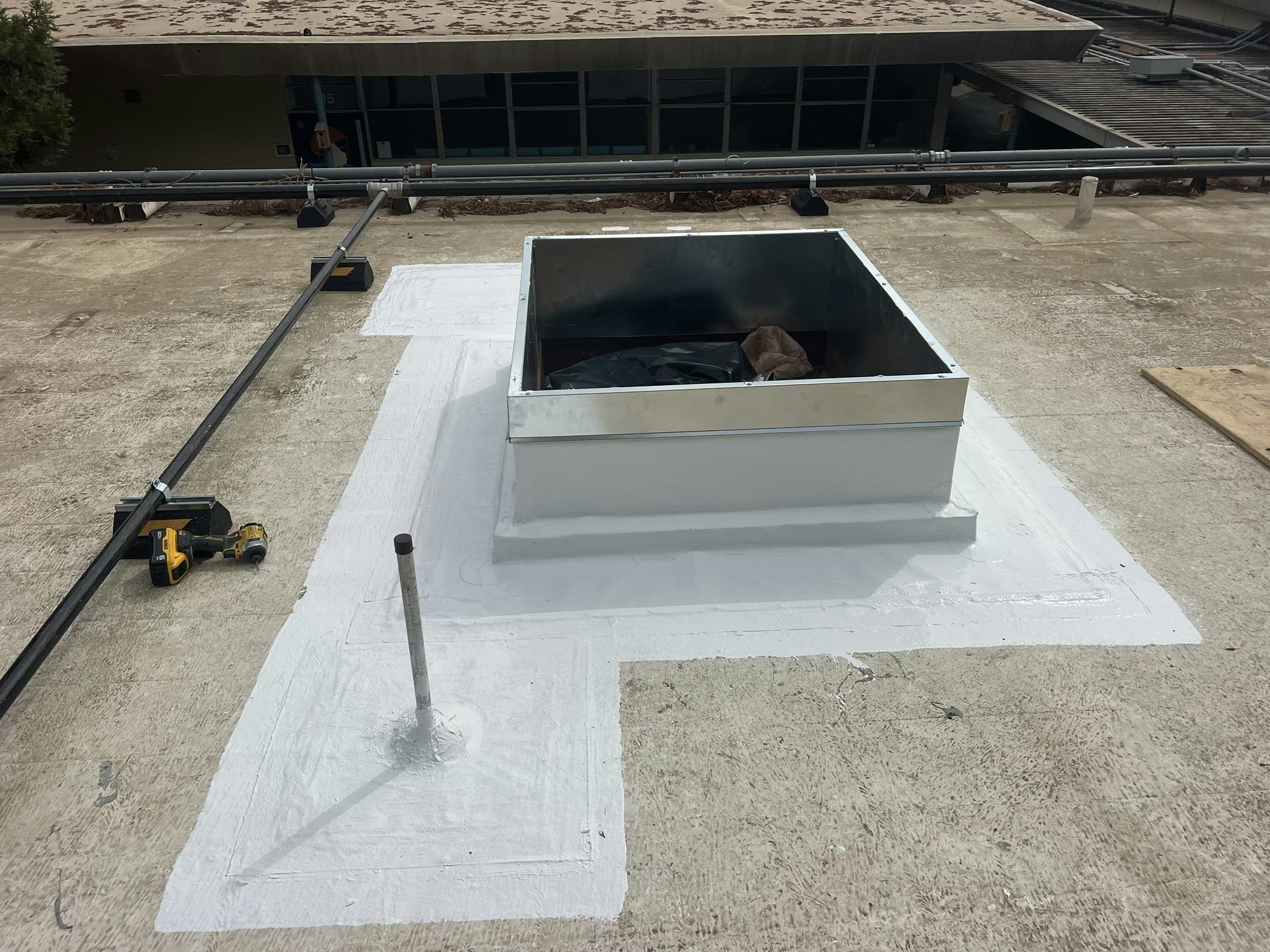 A rooftop with a metal box structure, pipes, a drill, and a white-painted section.