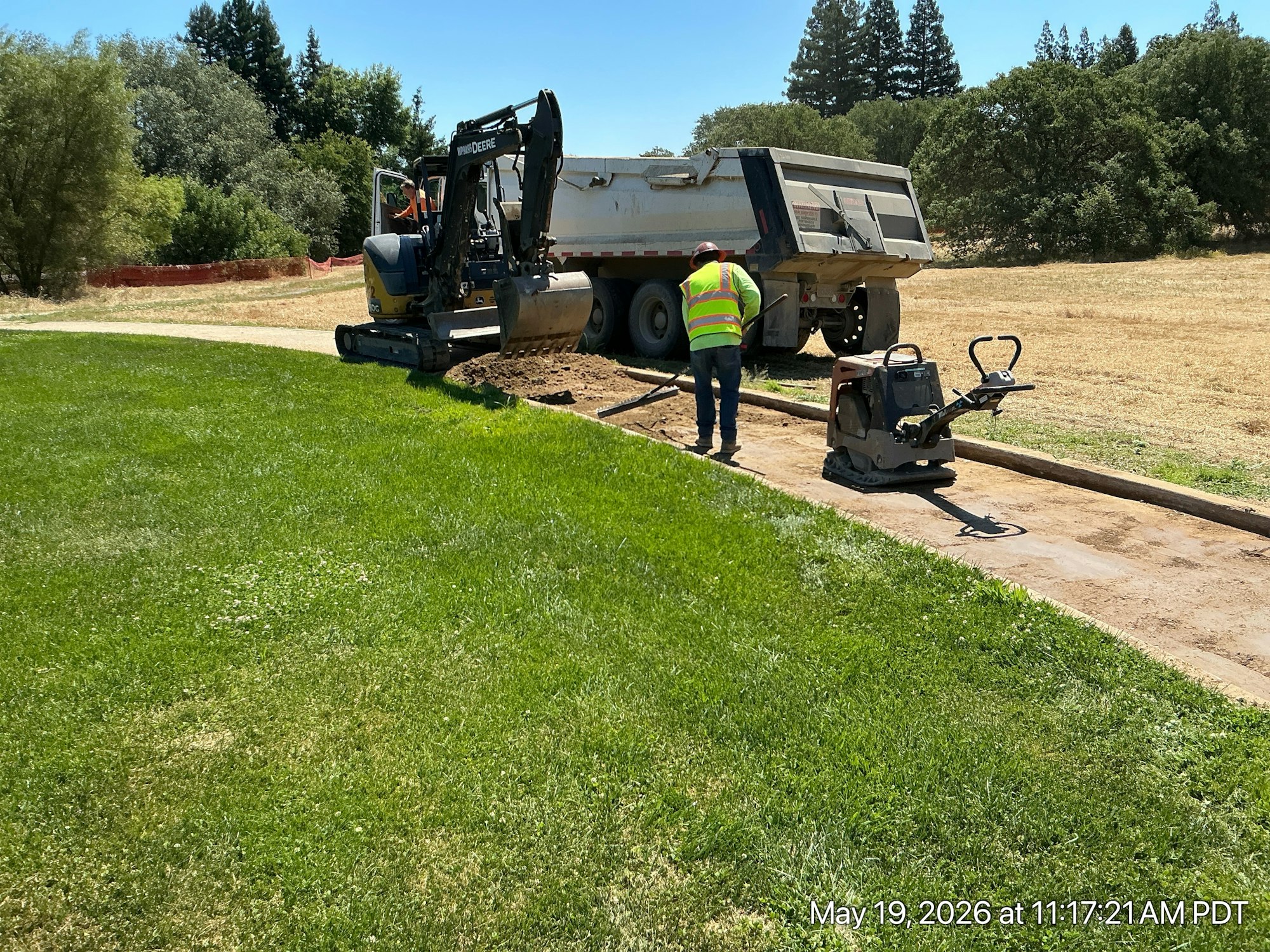 Workers operating machinery next to a truck on a grass field, likely performing landscaping or construction work.