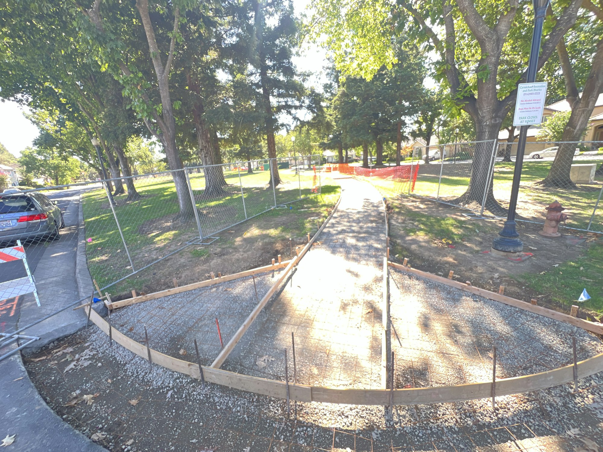 A pathway under construction with barriers, surrounded by trees and grass.