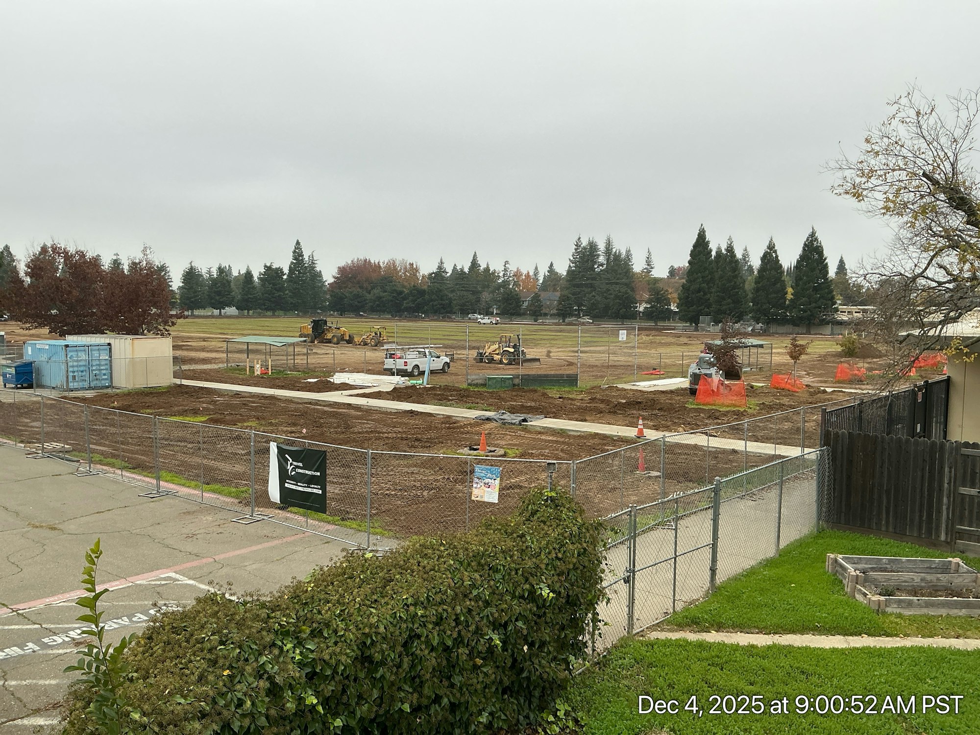 Construction site with equipment, a fenced area, and cloudy weather; ground is prepared for development.
