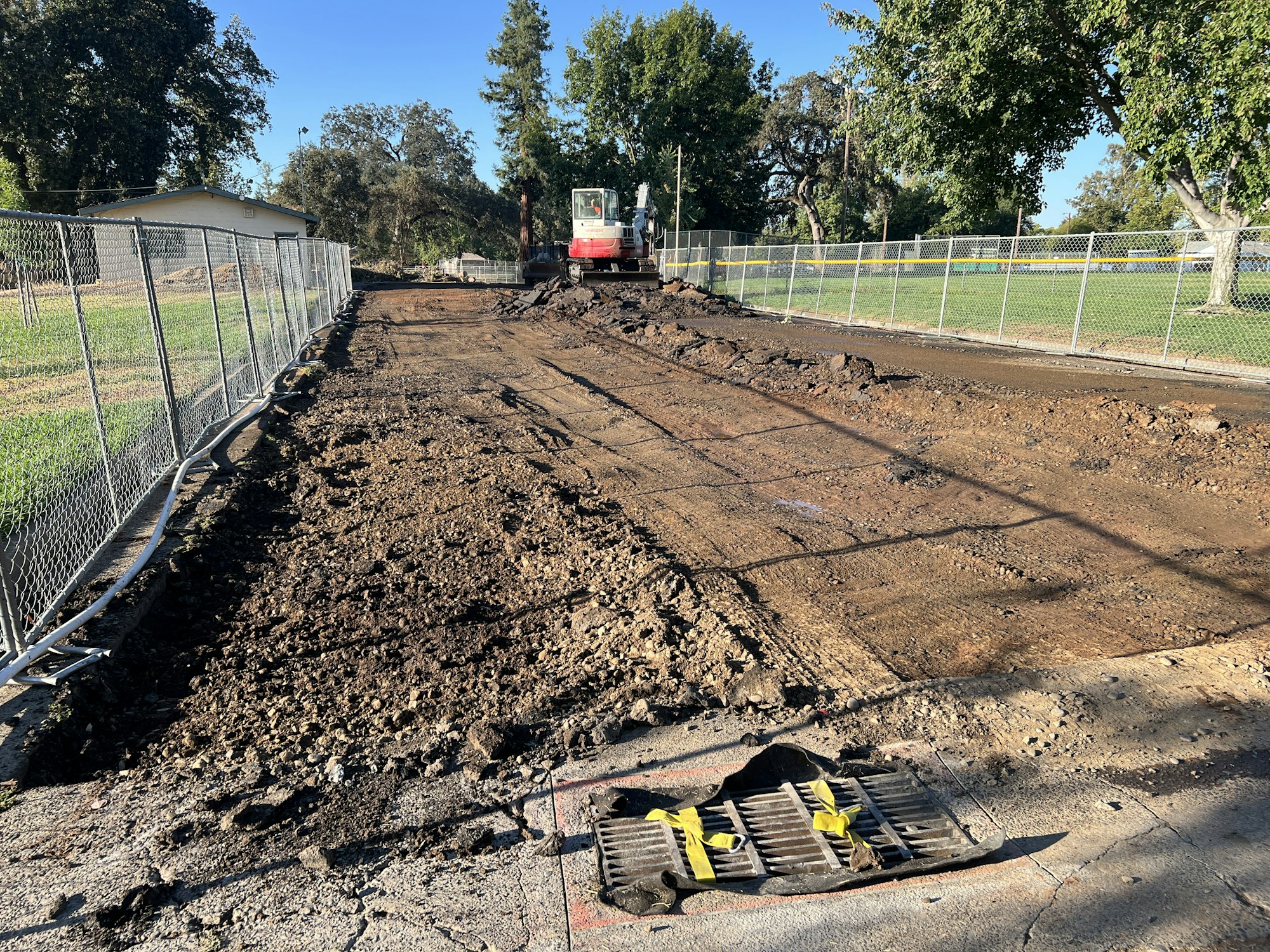 Construction site with dirt, fencing, and an excavator in the background.