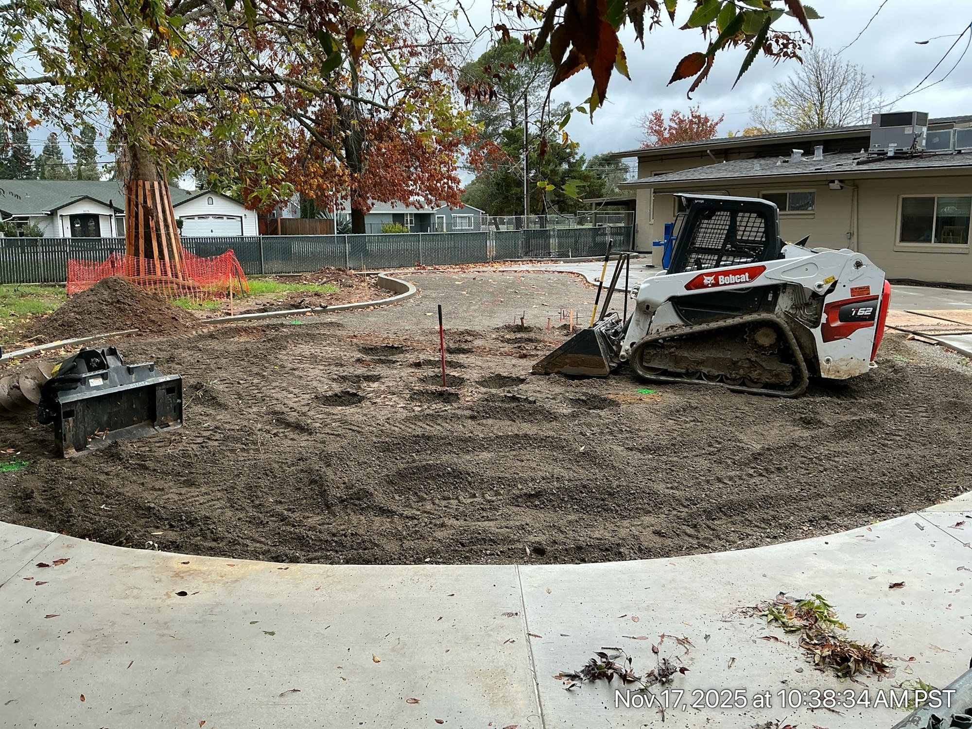 A construction area with a Bobcat machine, recently disturbed soil, and surrounding trees, likely for landscaping or site development.