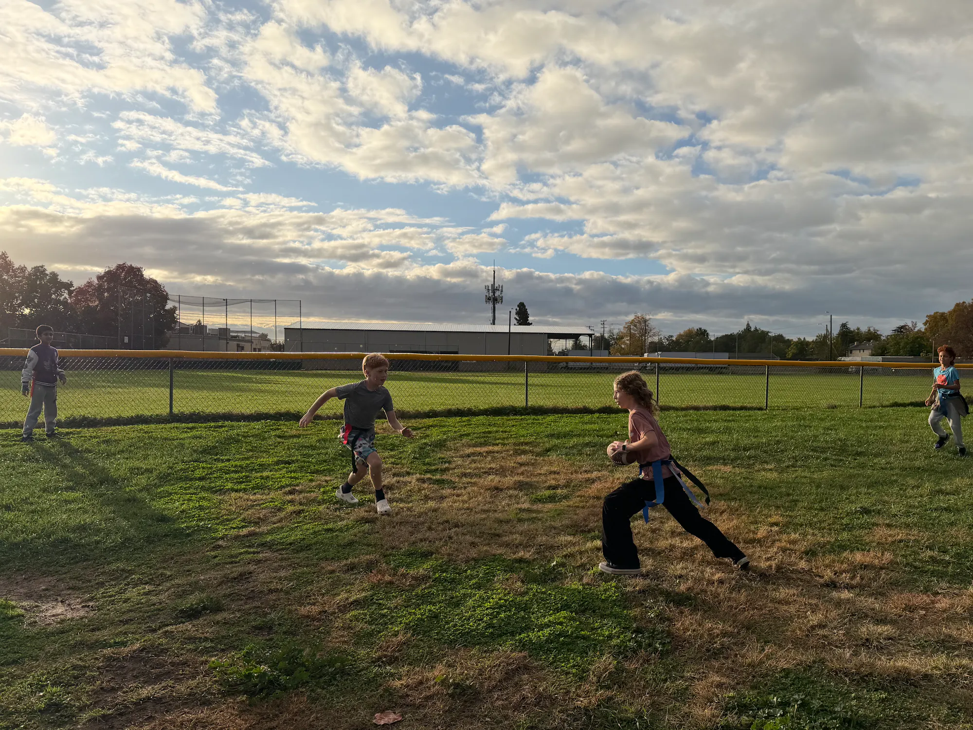 Kids playing outdoors on a grassy field, engaging in a game, with a cloudy sky in the background.