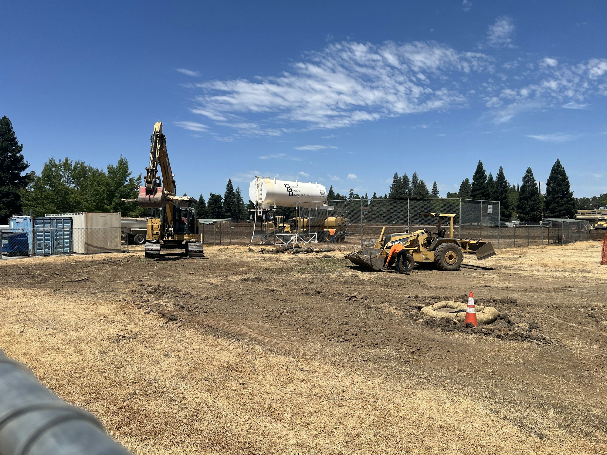 Construction site with heavy machinery, equipment, and a storage tank on dirt terrain.