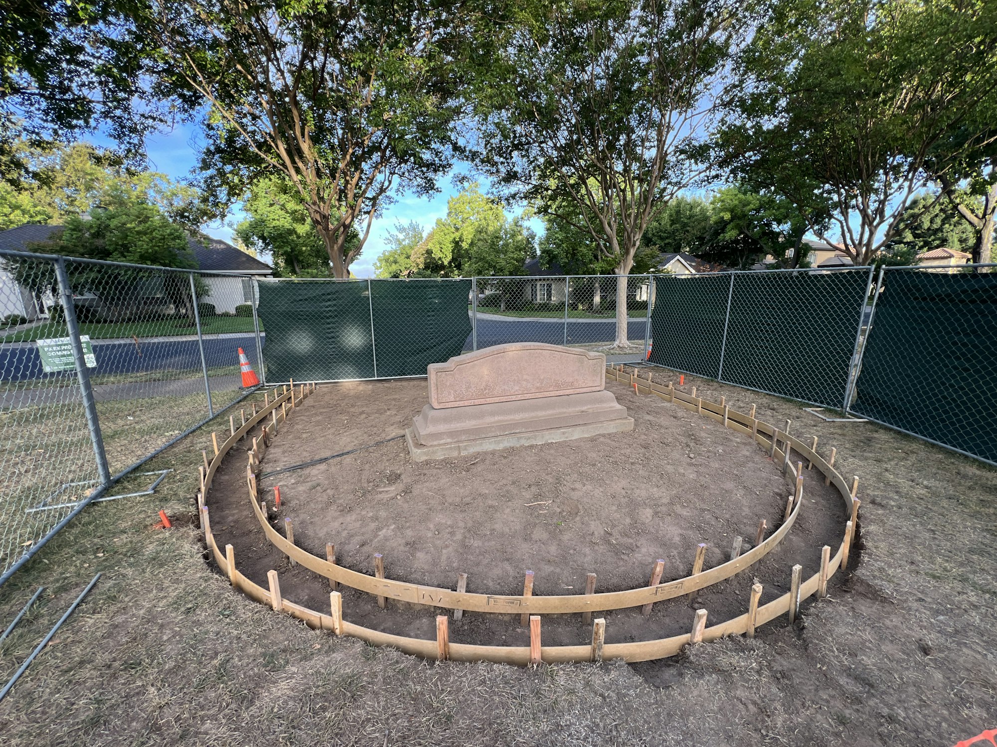A fenced-off area with a circular wooden frame surrounding a monument, likely for construction or landscaping.