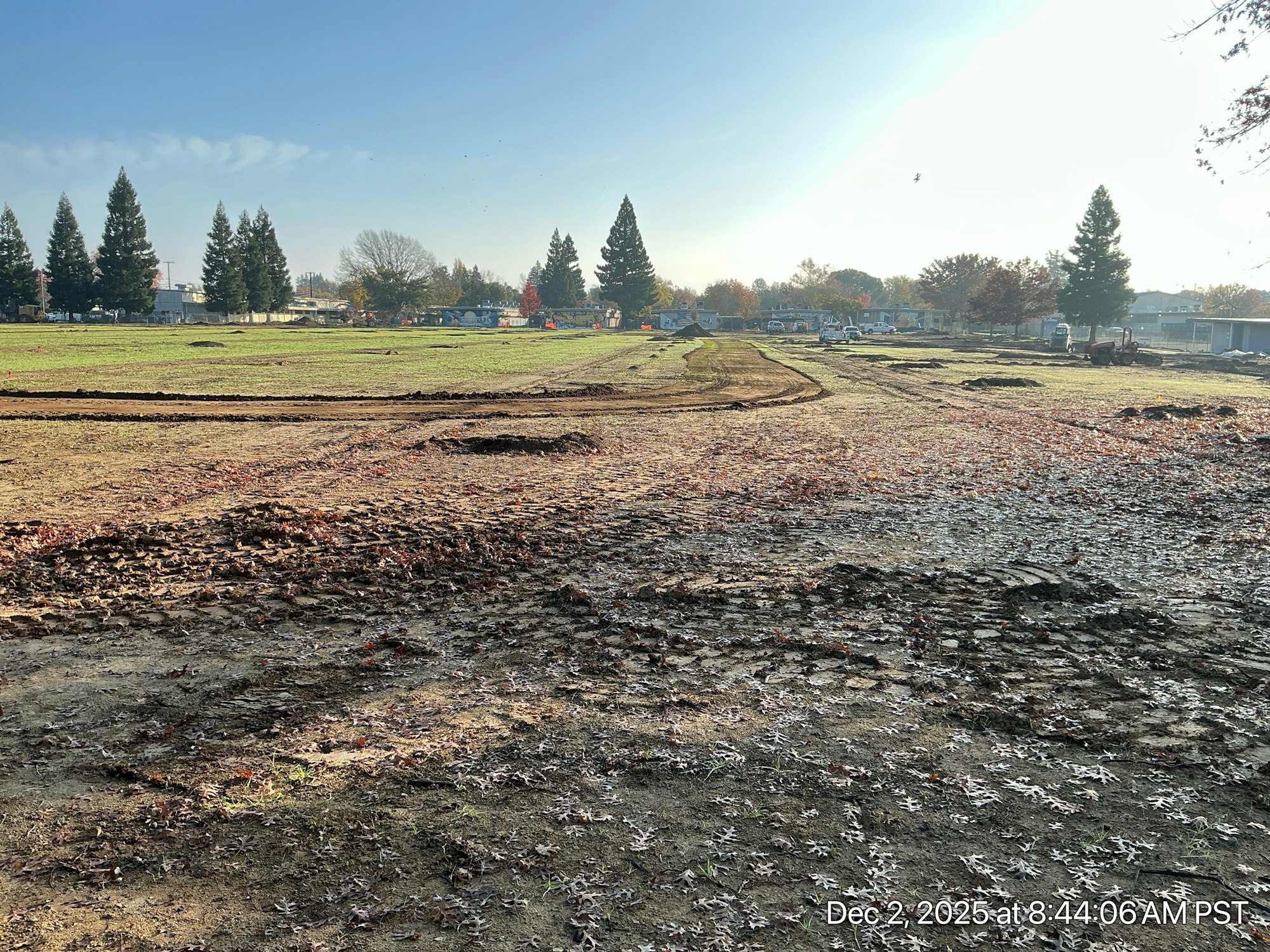 The image shows a cleared field with muddy ground, tire tracks, and scattered leaves under a clear sky.