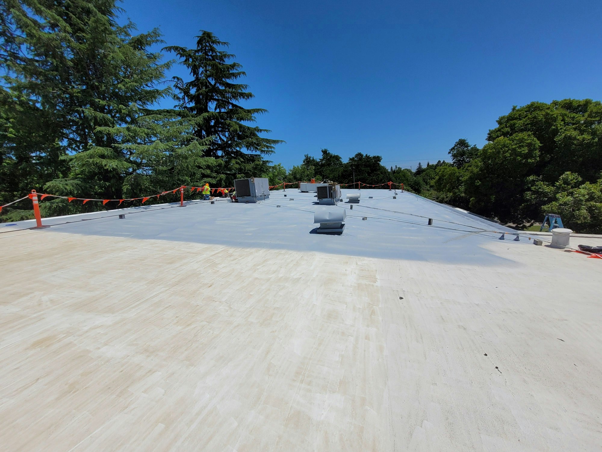 Flat roof with HVAC units, safety barrier tape, and trees in the background.