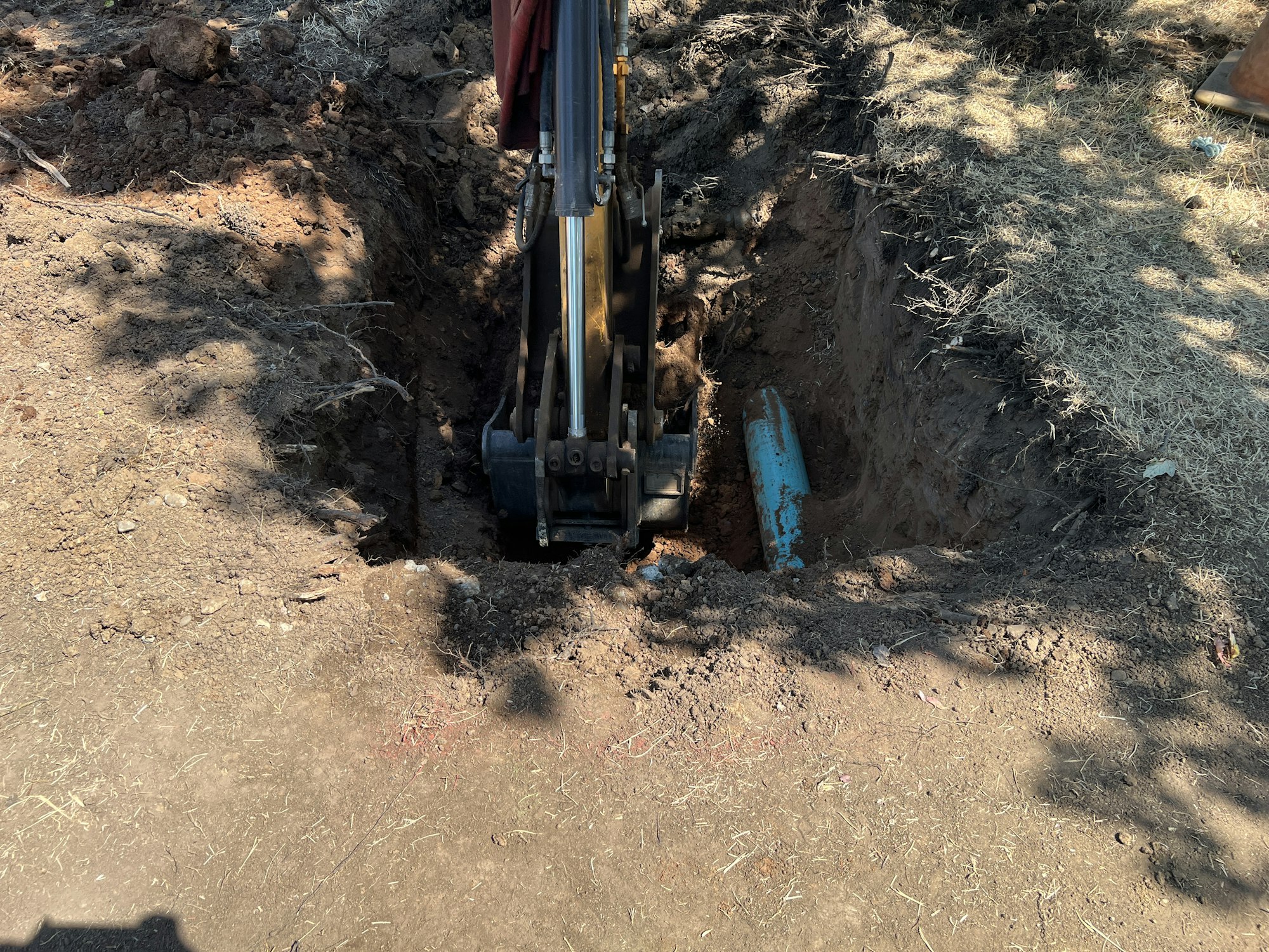 A backhoe digging a trench, exposing a section of blue pipe underground.