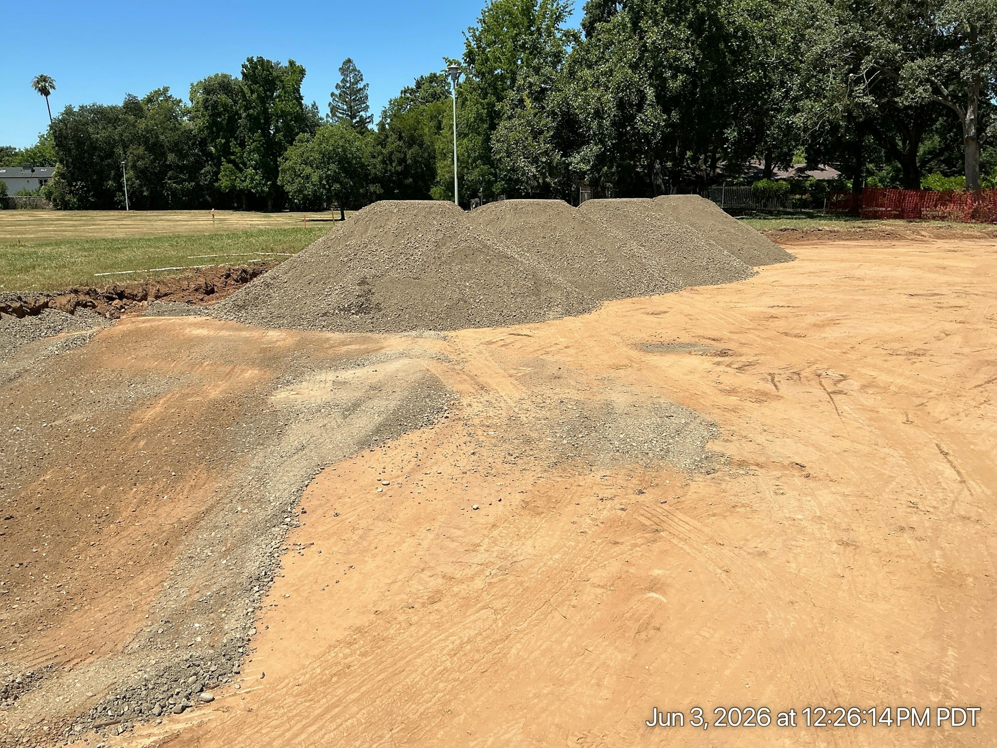 The image shows a construction site with piles of gravel or dirt and a clear blue sky in the background.