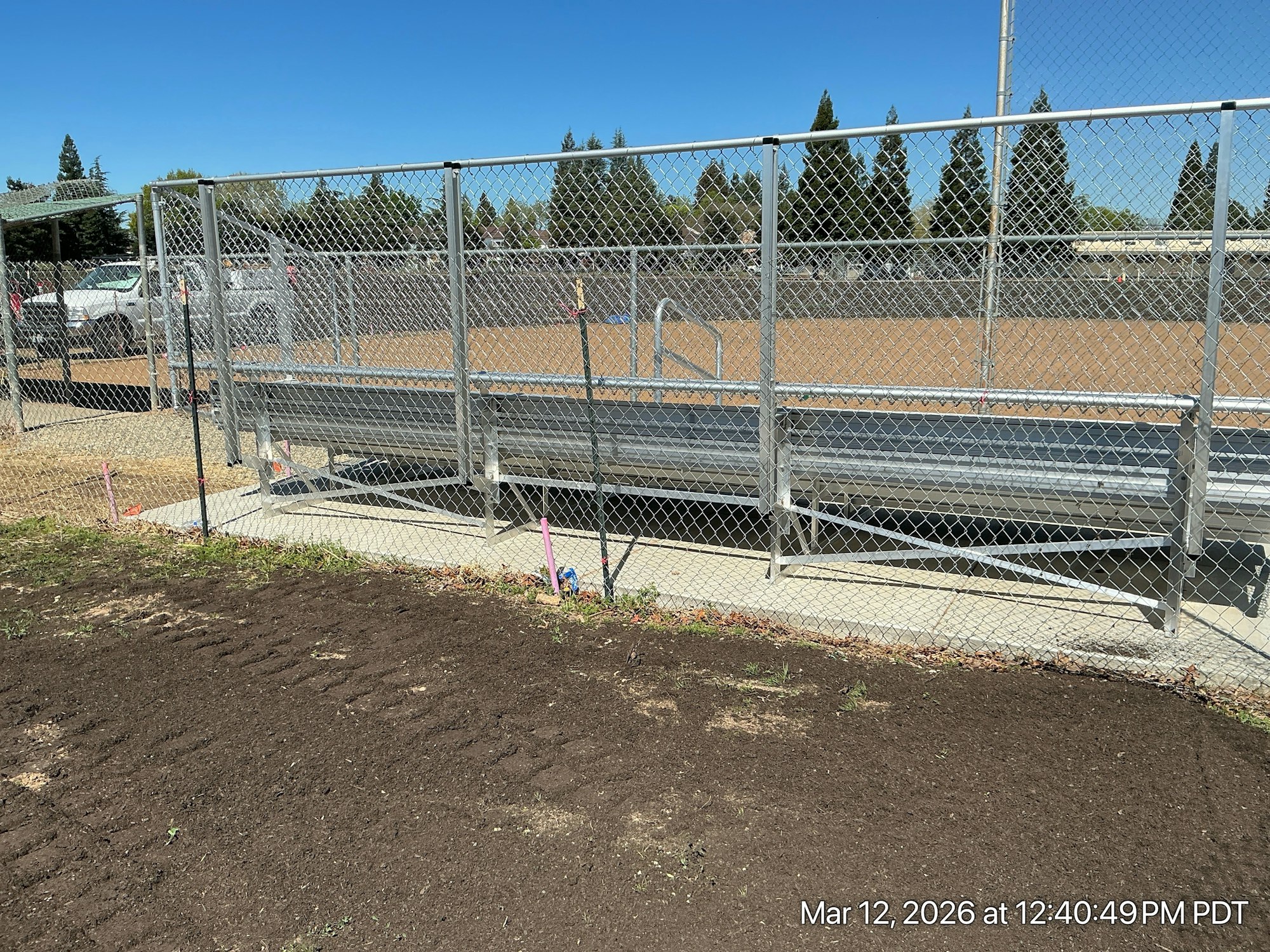 The image shows a fenced area with a metal platform and a dirt surface, likely for a sports field or a similar facility.