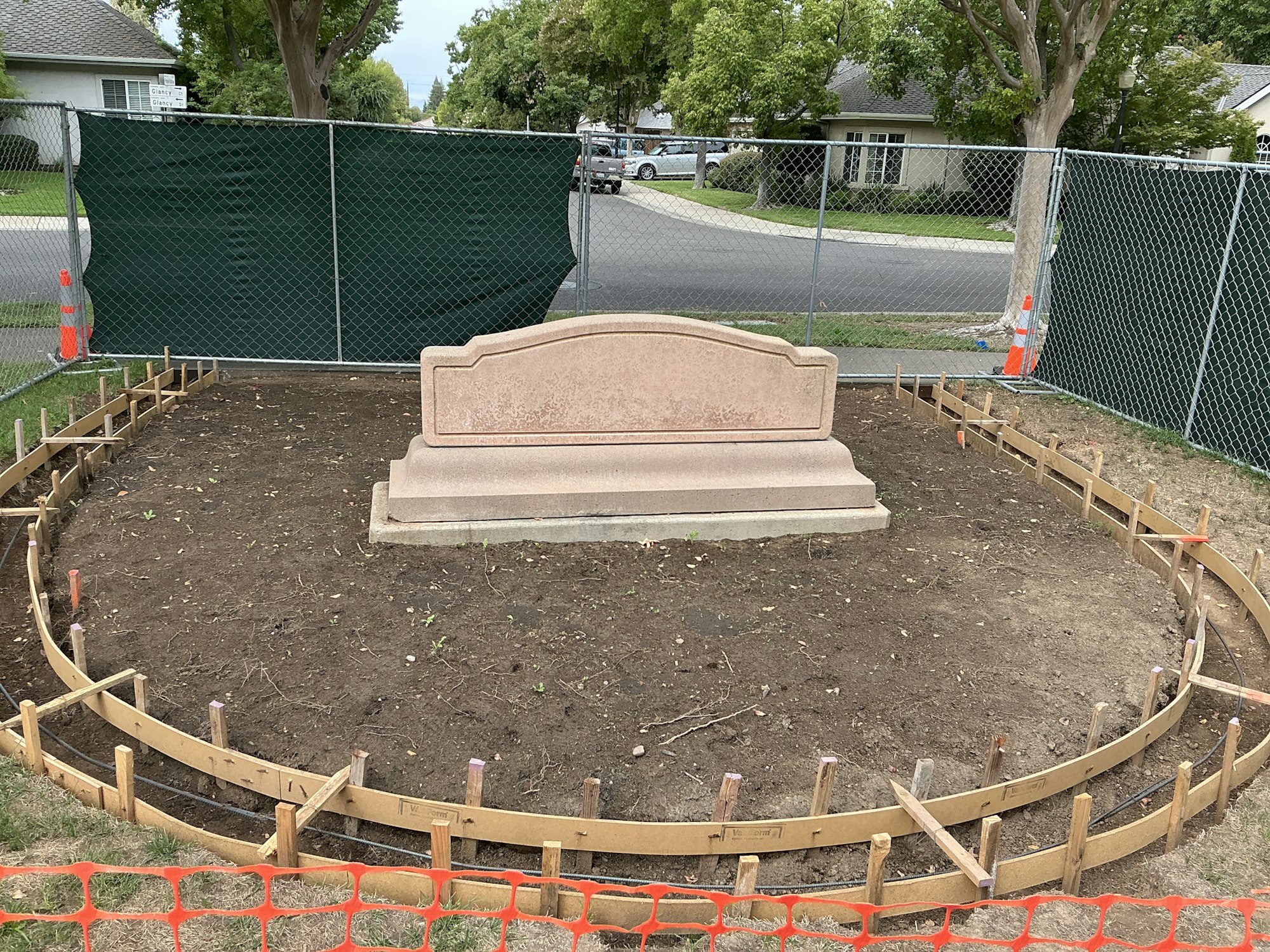 A mounted plaque surrounded by dirt and wooden framing, with a chain-link fence in the background.