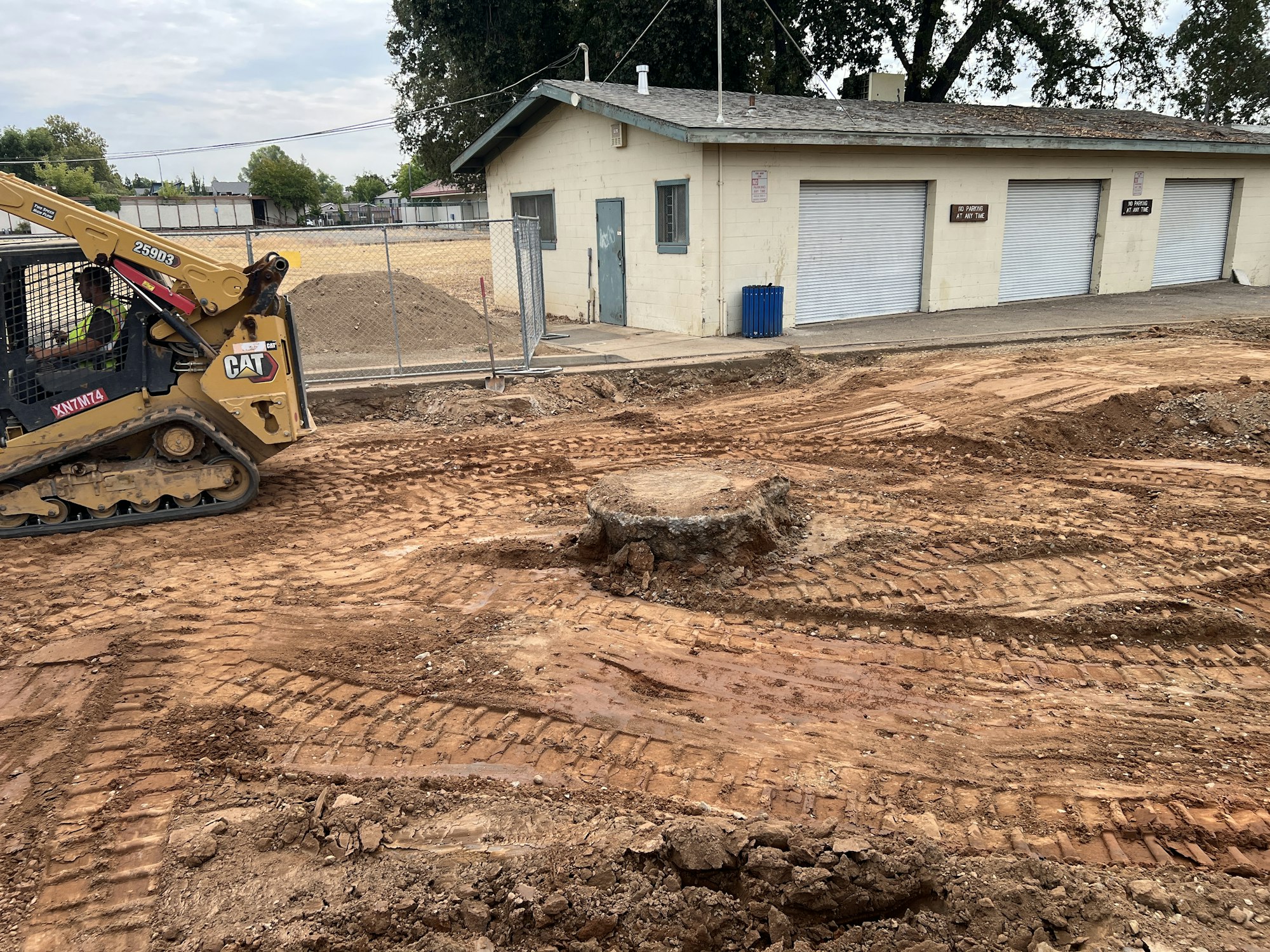 Construction site with a bulldozer in front of a building, dirt tracks visible.