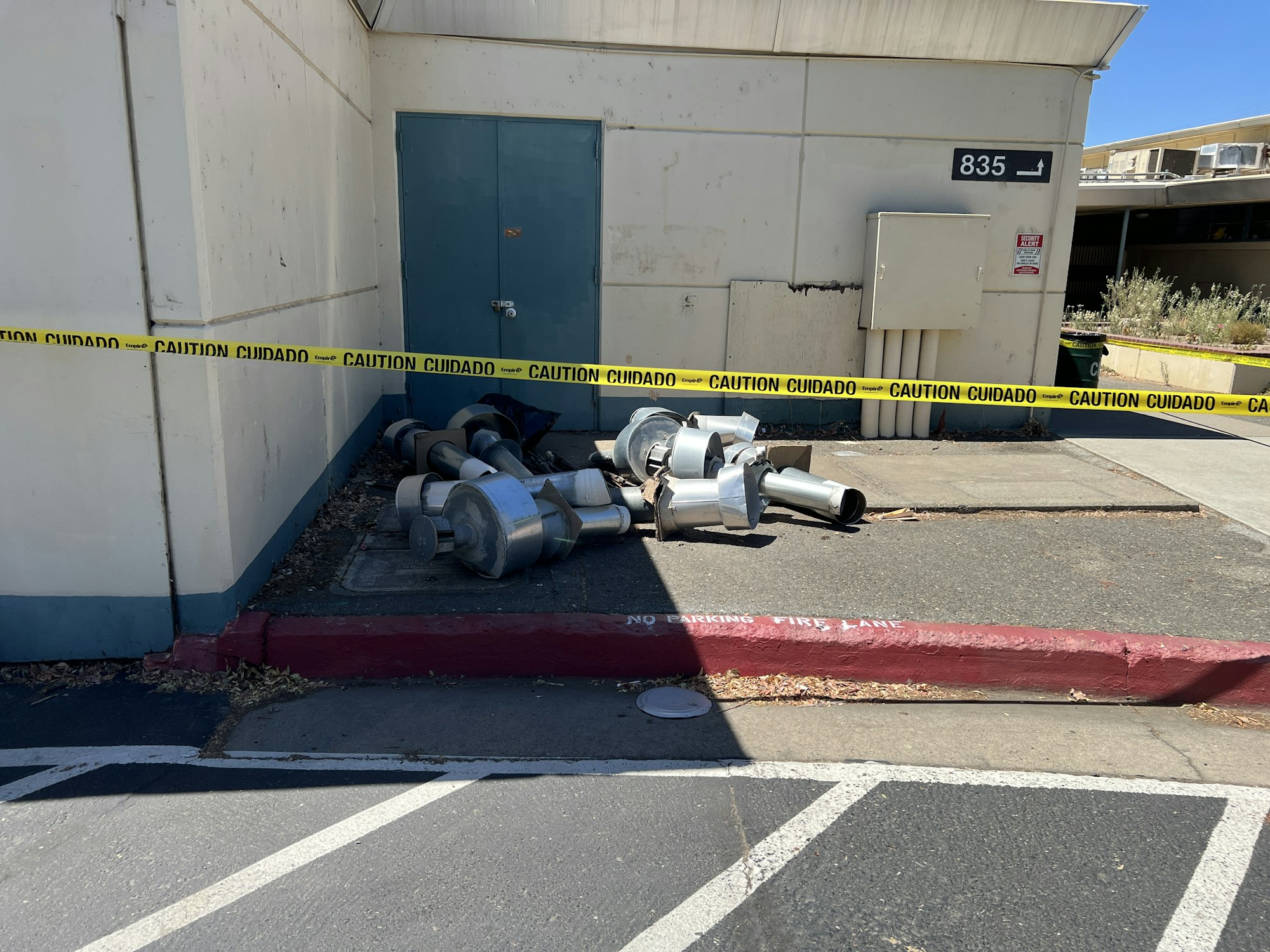 Metallic ducts on the ground near a building, surrounded by caution tape.