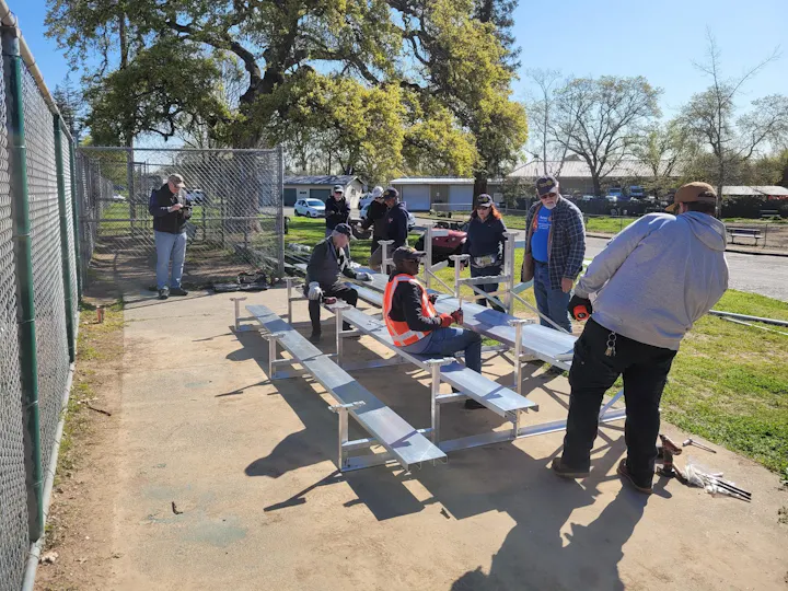 A group of people working together to assemble bleachers in a park on a sunny day.