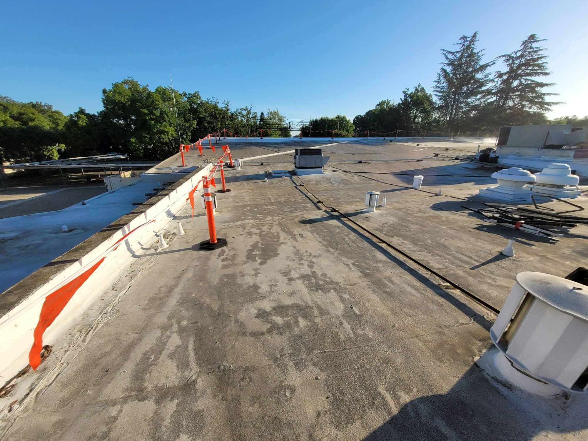 Flat commercial roof with vents, safety barrier cones, and clear skies.
