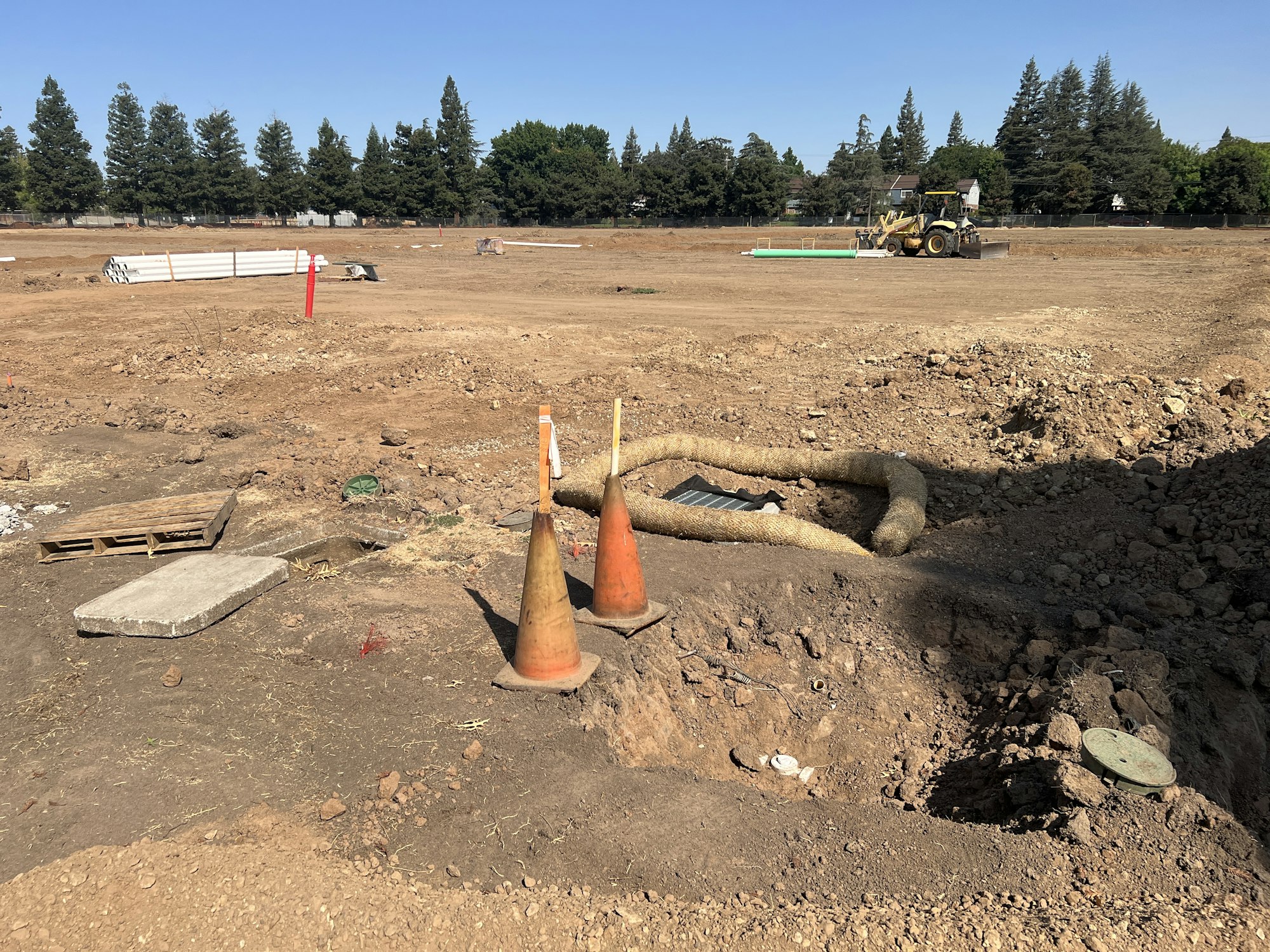 A construction site with dirt, traffic cones, a tractor, and building materials scattered on the ground.