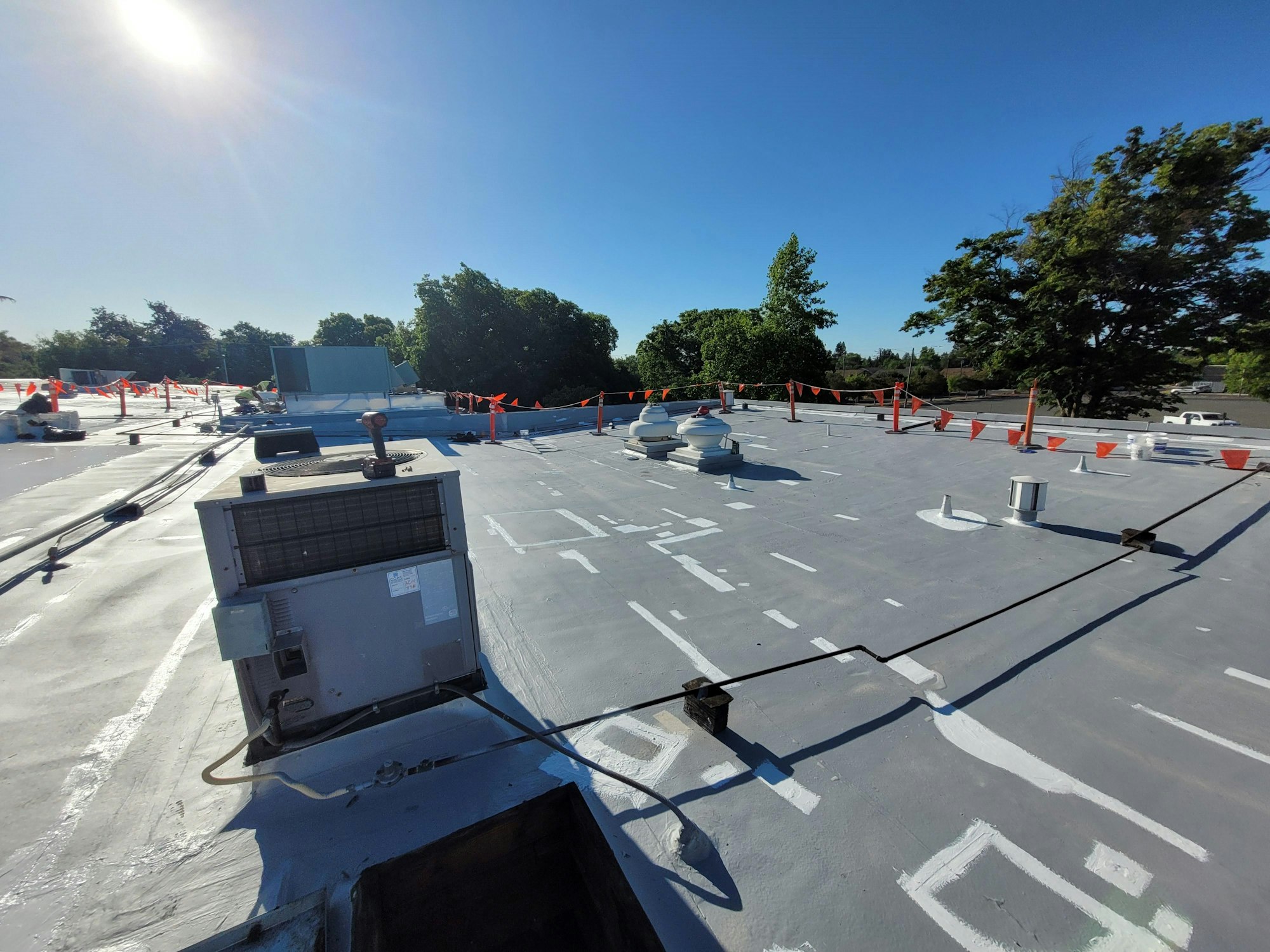 A commercial building rooftop with HVAC units, vents, safety cones, and a clear blue sky.